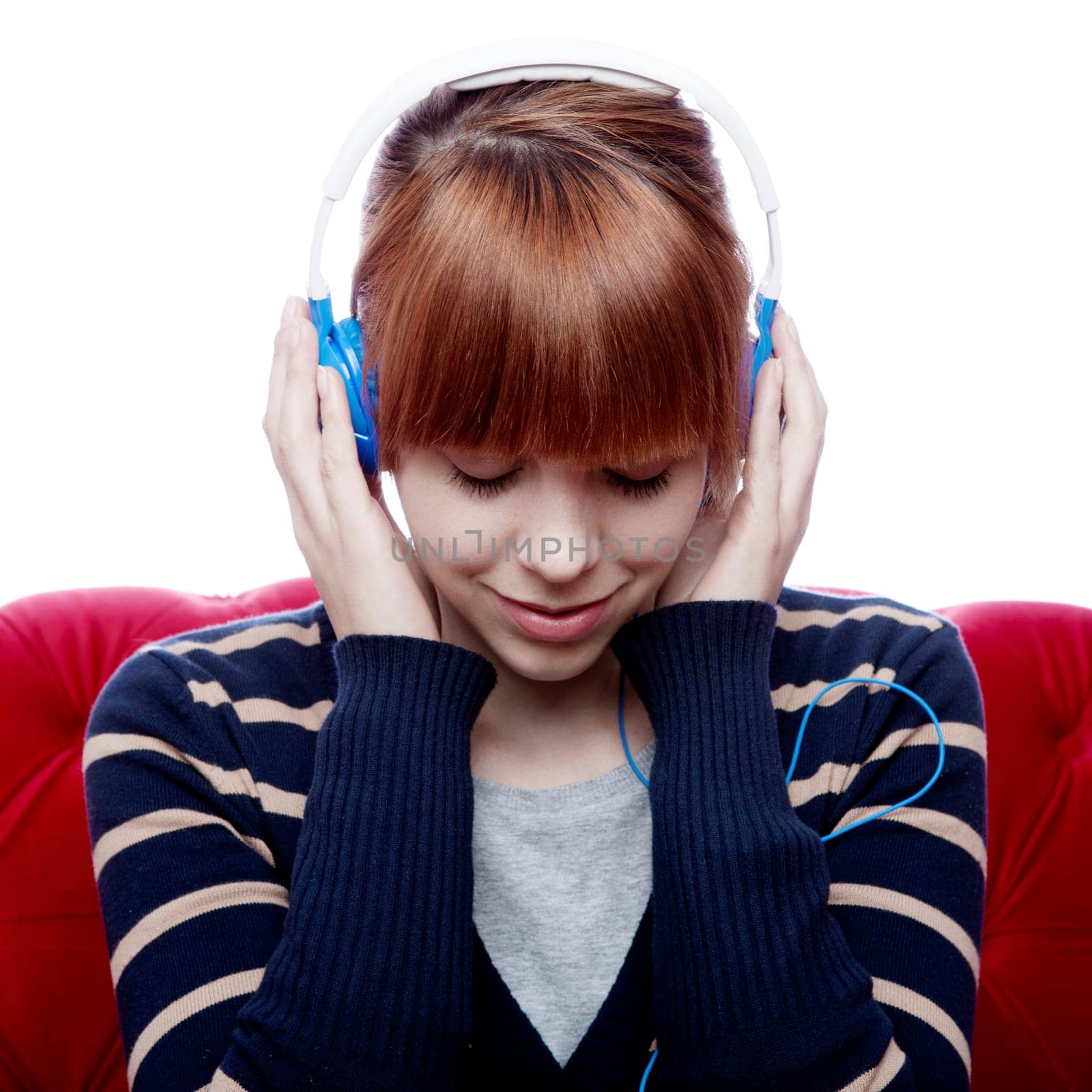 young beautiful red haired girl on red sofa listen to great music with headphones in front of white background