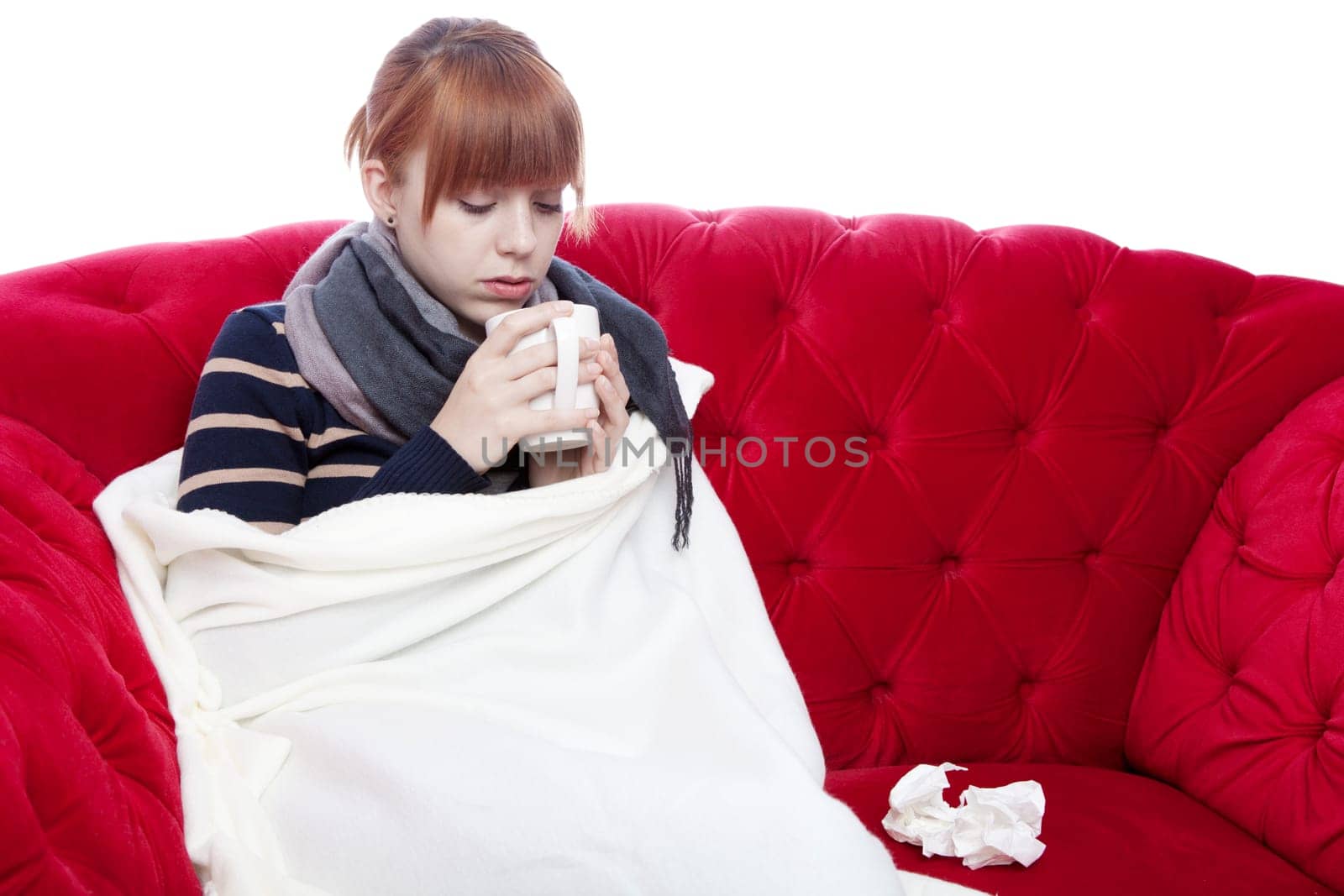 young beautiful red haired girl on red sofa has a cold in front of white background