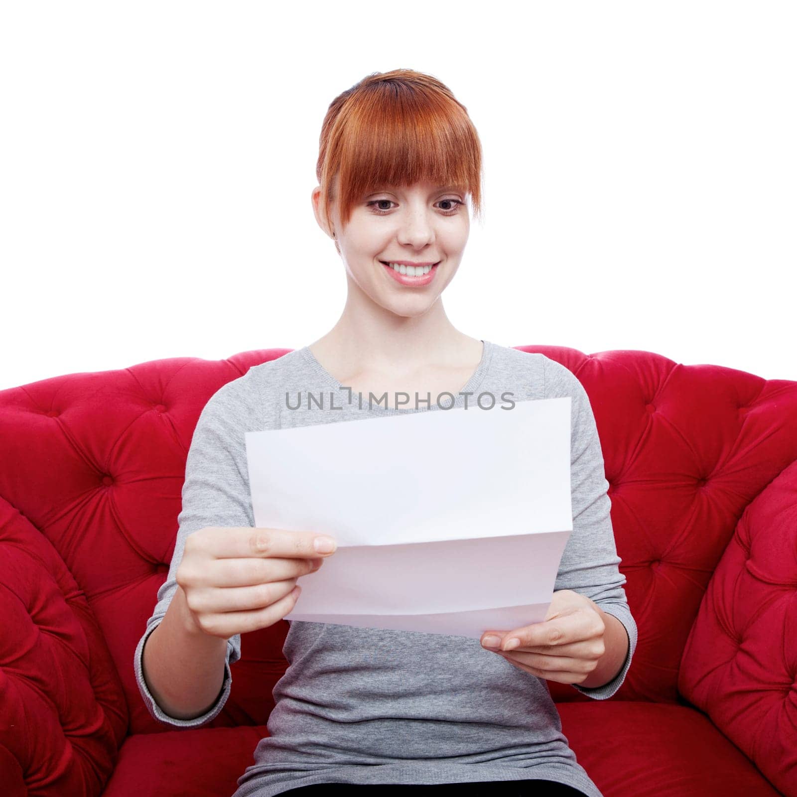 young beautiful red haired girl on red sofa reading a letter in front of white background
