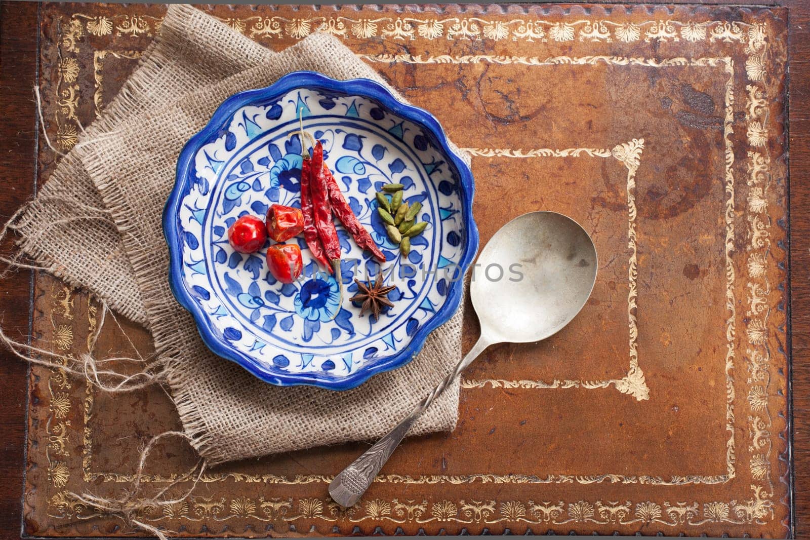 Cardamon seeds, star anise and peppers in a colorful blue bowl on a vintage table.