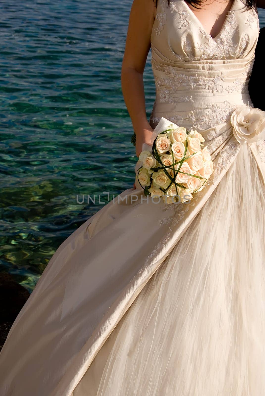 Bride holding wedding bouquet. Blue sea in the background.