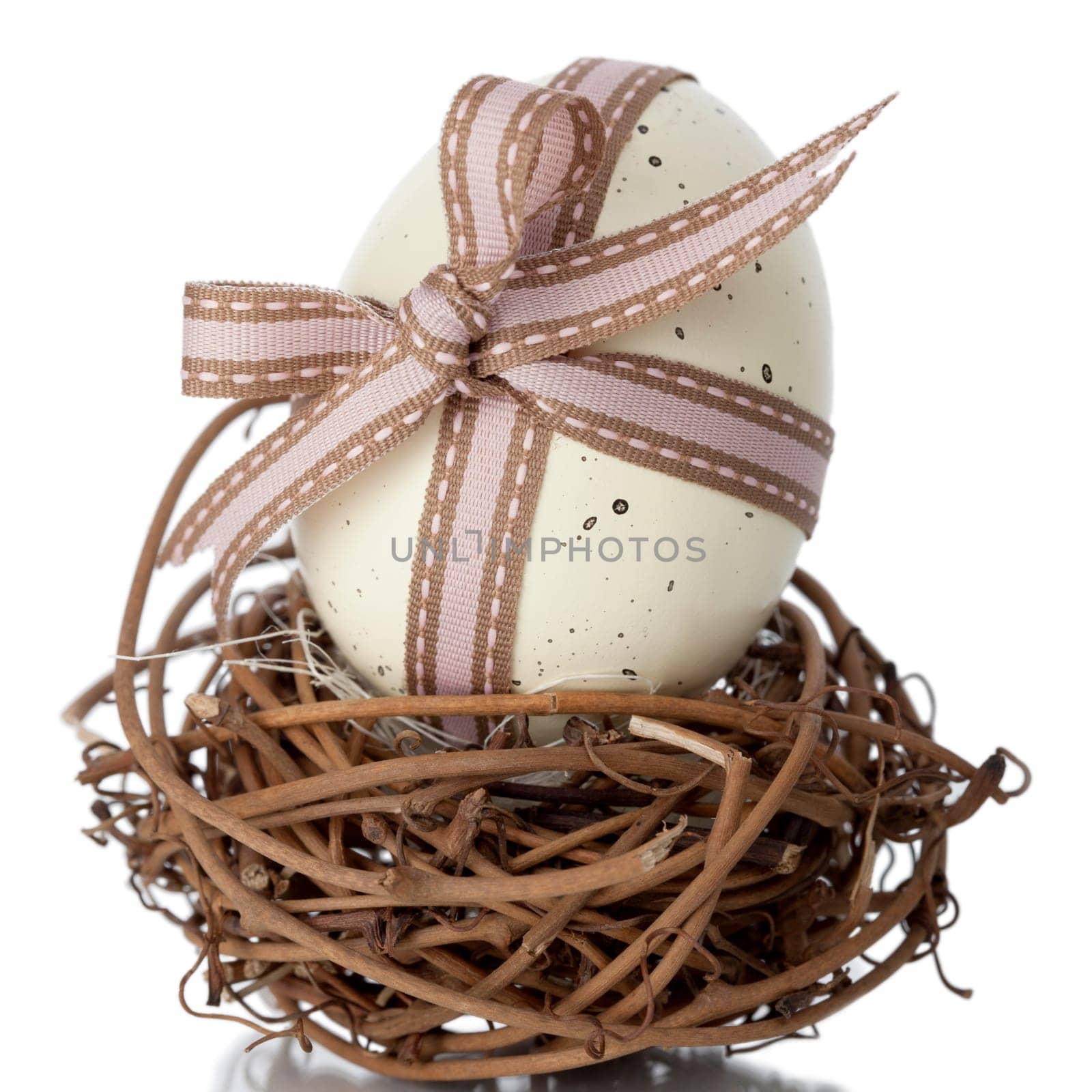 EasterEgg tied in a bow with ornamental ribbon balanced on a small nest of interwoven twigs against a white studio background