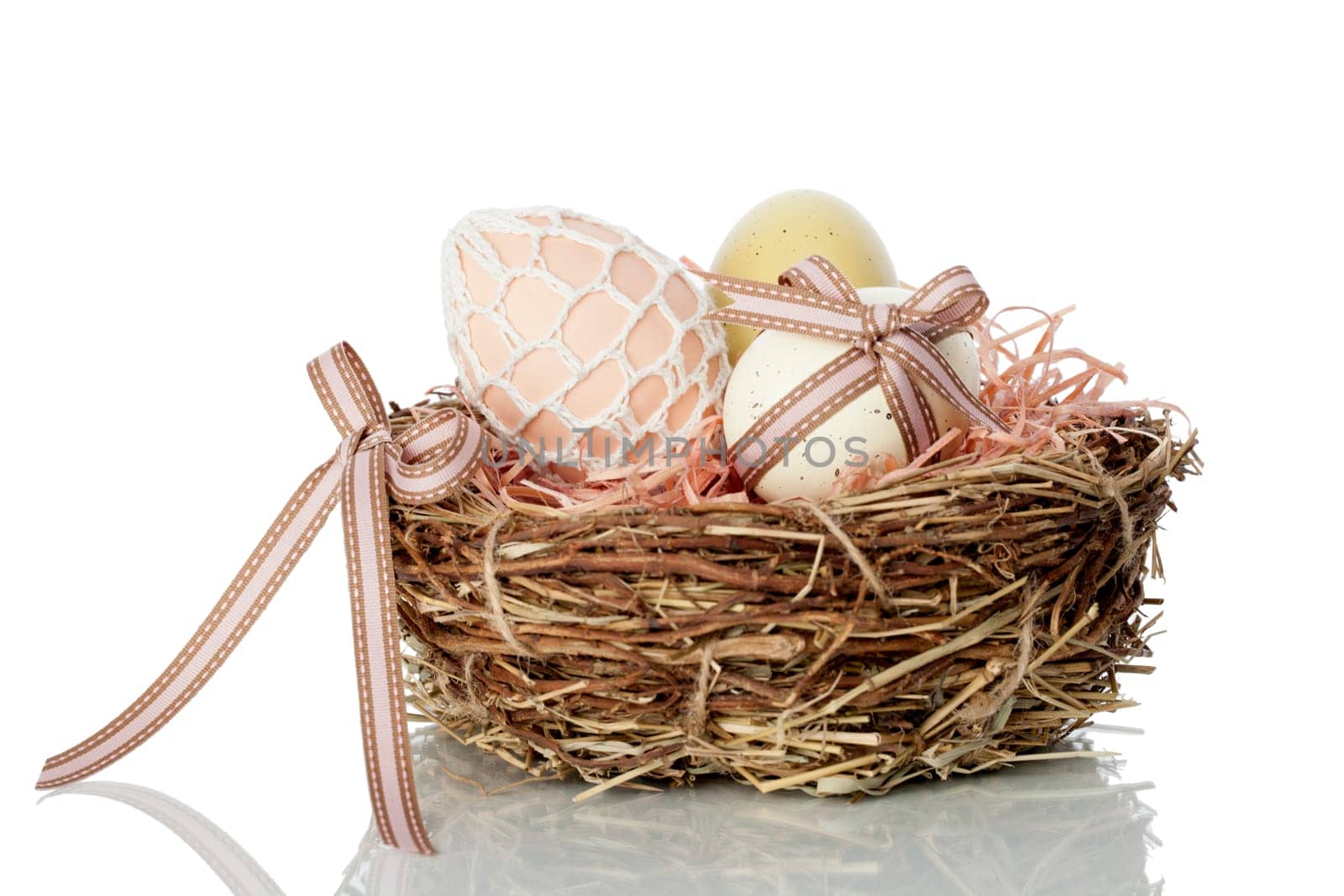 Neat straw and twig nest full of traditional hand decorated Easter Eggs on a white studio background