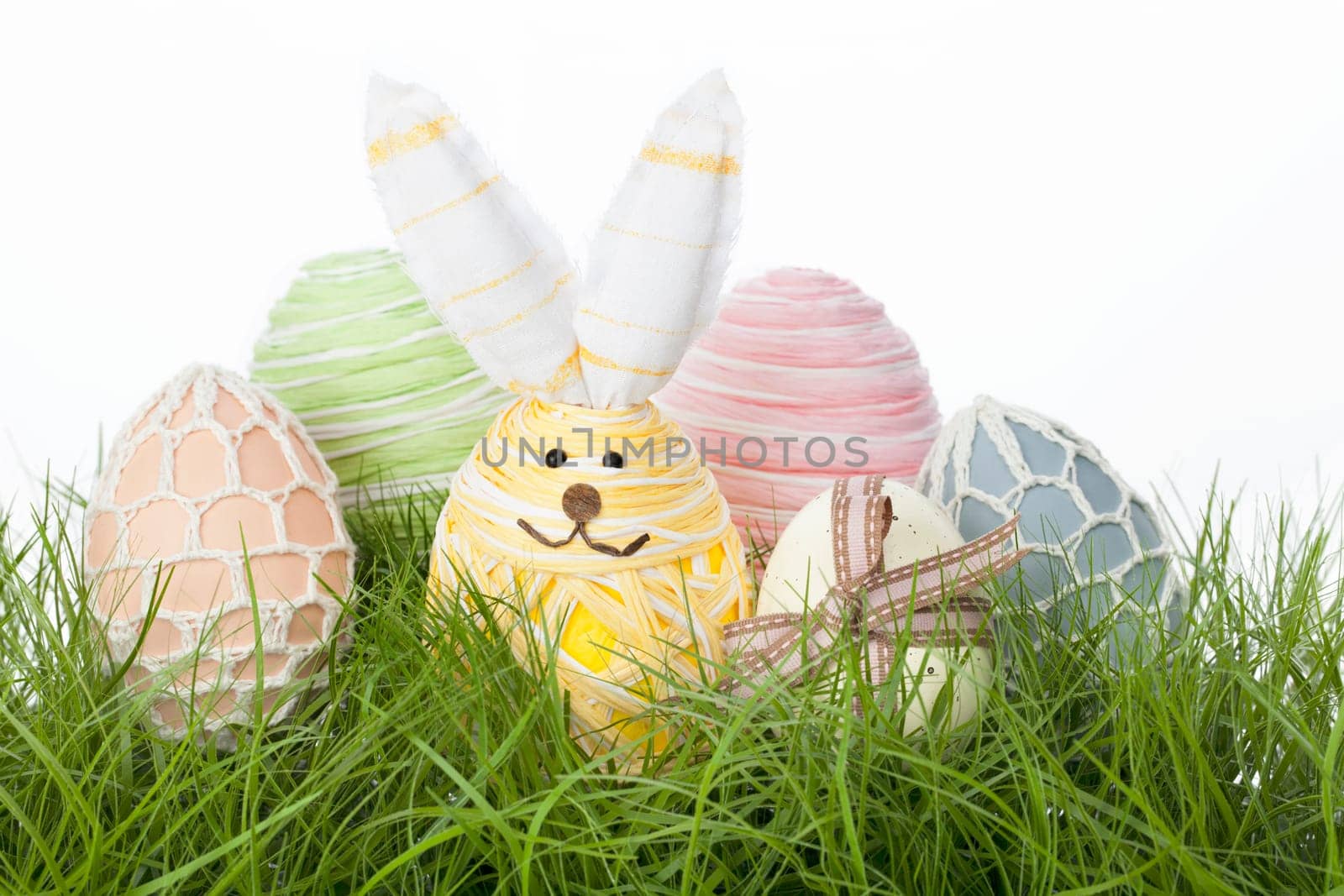 Collection of delicate pastel country Easter Eggs handcrafted with raffia, tied with a bow, covered in netting or fashioned into an adorable Easter bunny, nestling in fresh green grass