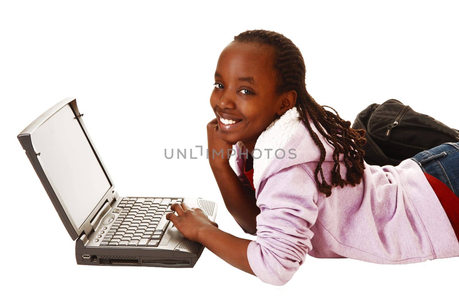 A young pretty black teen girl lying on the floor with her laptop smiling into the camera, for white background.