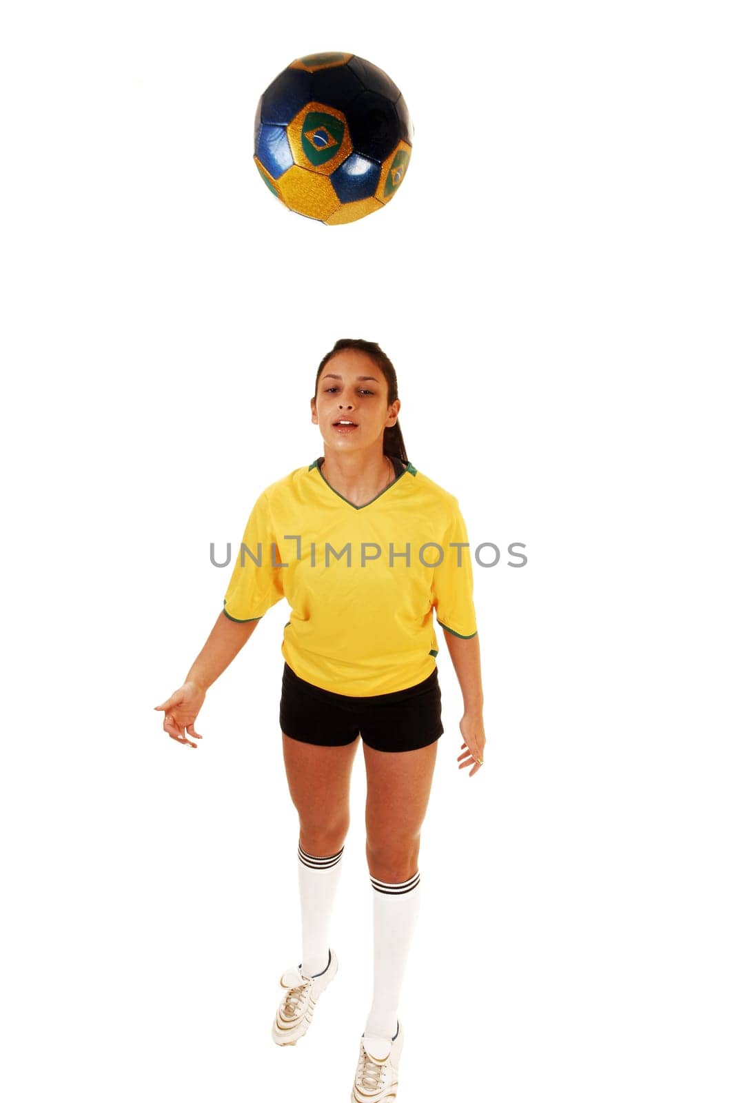A pretty teenage girl standing in the studio in her soccer uniform and playing with the football, her hair in a ponytail for white background.