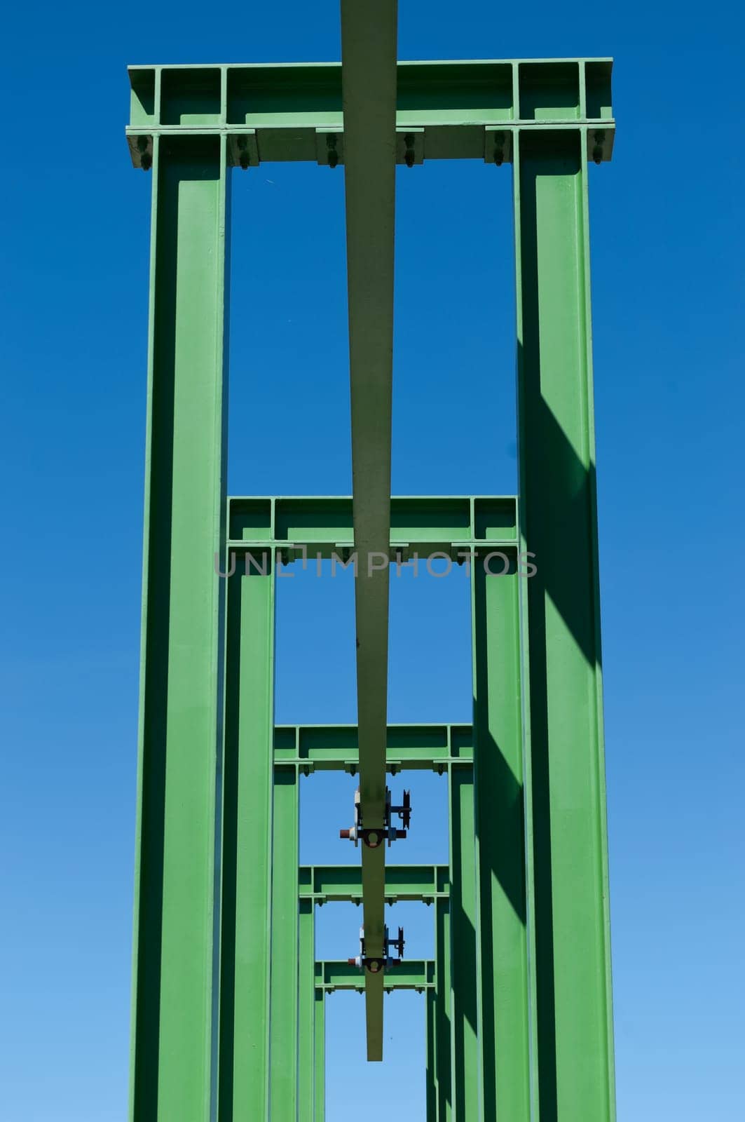 Detail of a small gantry crane painted green against the blue sky