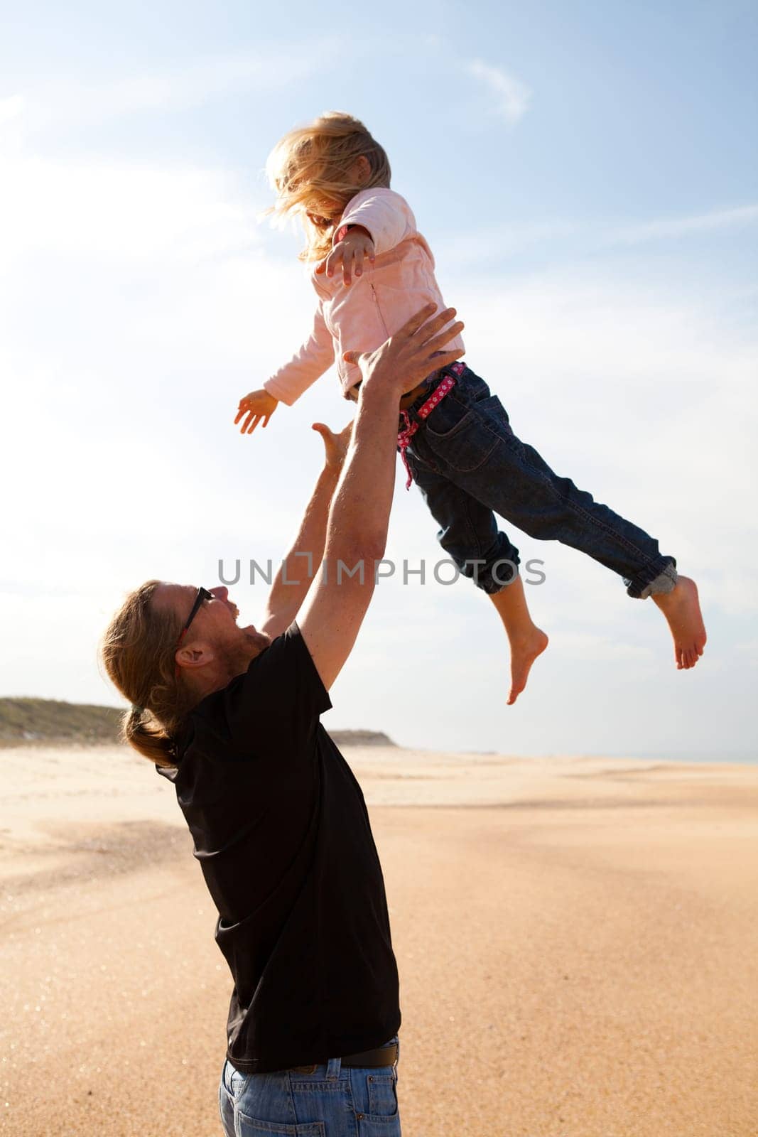 Father throwing young daughter into the air at beach while on vacation