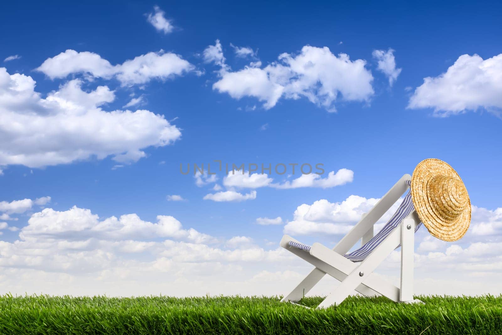 Sun chair with straw hat in front of blue sky on lawn