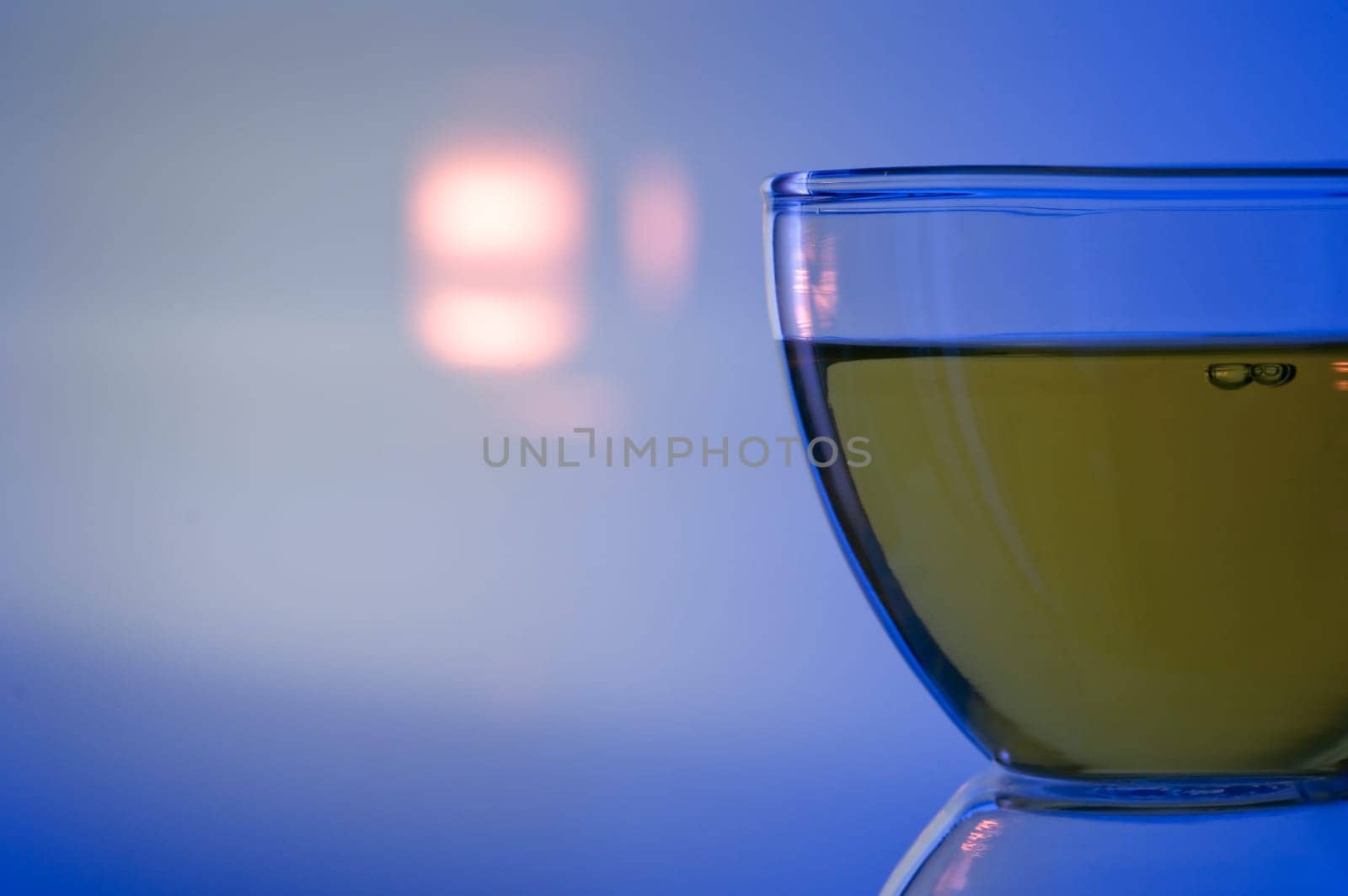 Close studio shot of a filled tea glass in the foreground with background projection of a backlight on blue background