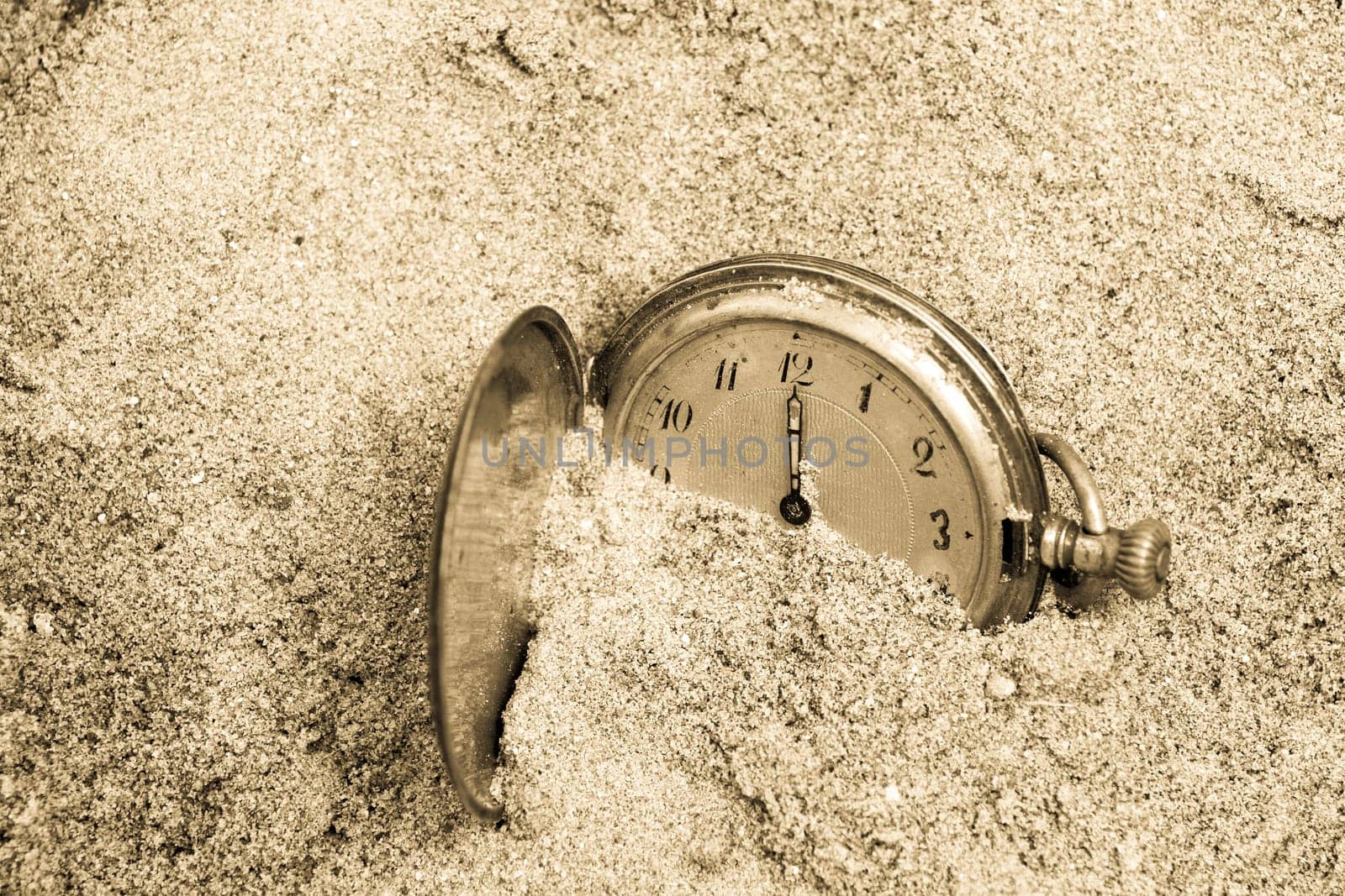 Old pocket watch lying in sand. Time concept.