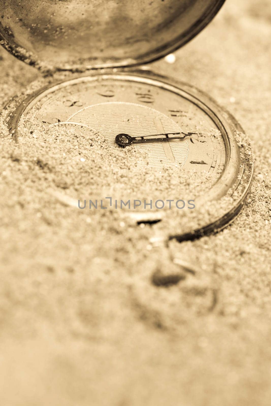 Old pocket watch lying in sand. Time concept.