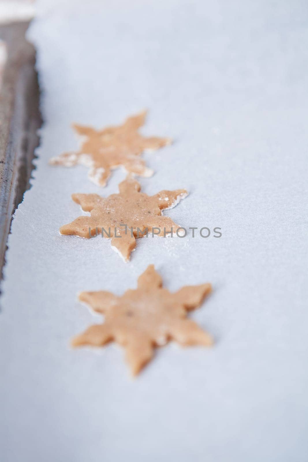 Closeup of three pieces of star shaped gingerbread dough on baking paper