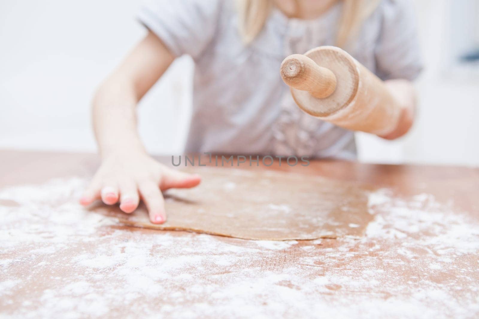 Young girl working on dough with hands and wooden rolling pin to make gingerbread biscuits