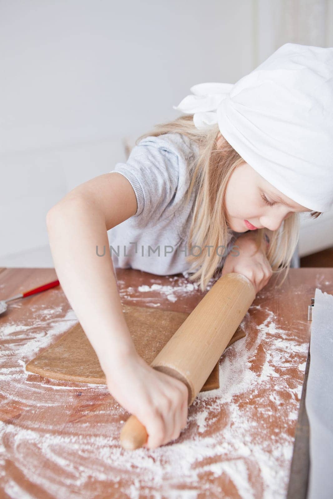 Young girl working on dough with rolling pin to make gingerbread biscuits