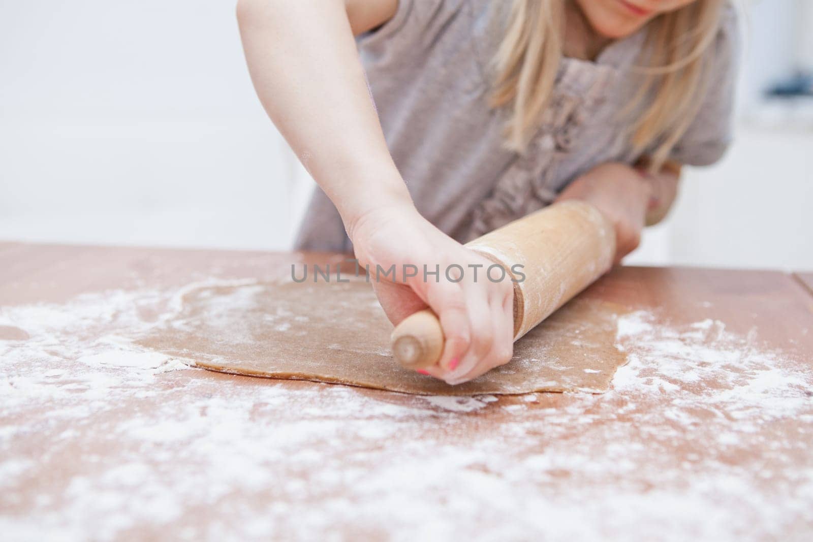 Young girl working on dough with rolling pin to make gingerbread biscuits