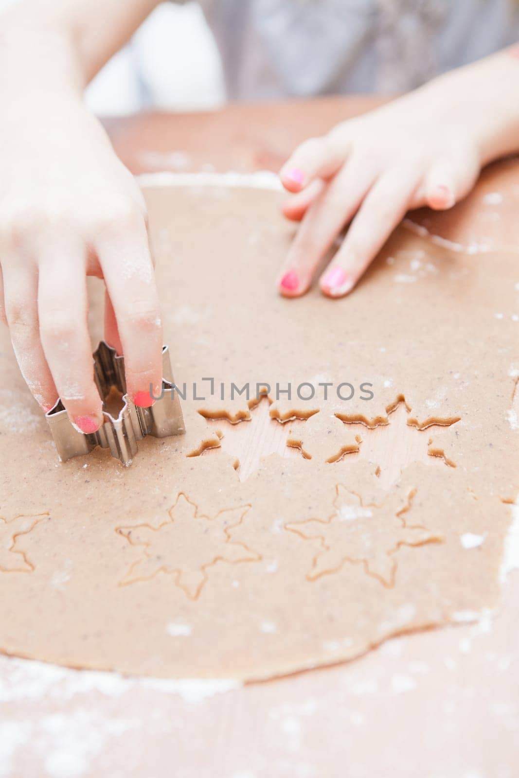 Closeup of hand of young girl making star shaped gingerbread biscuits with metal cutter from dough