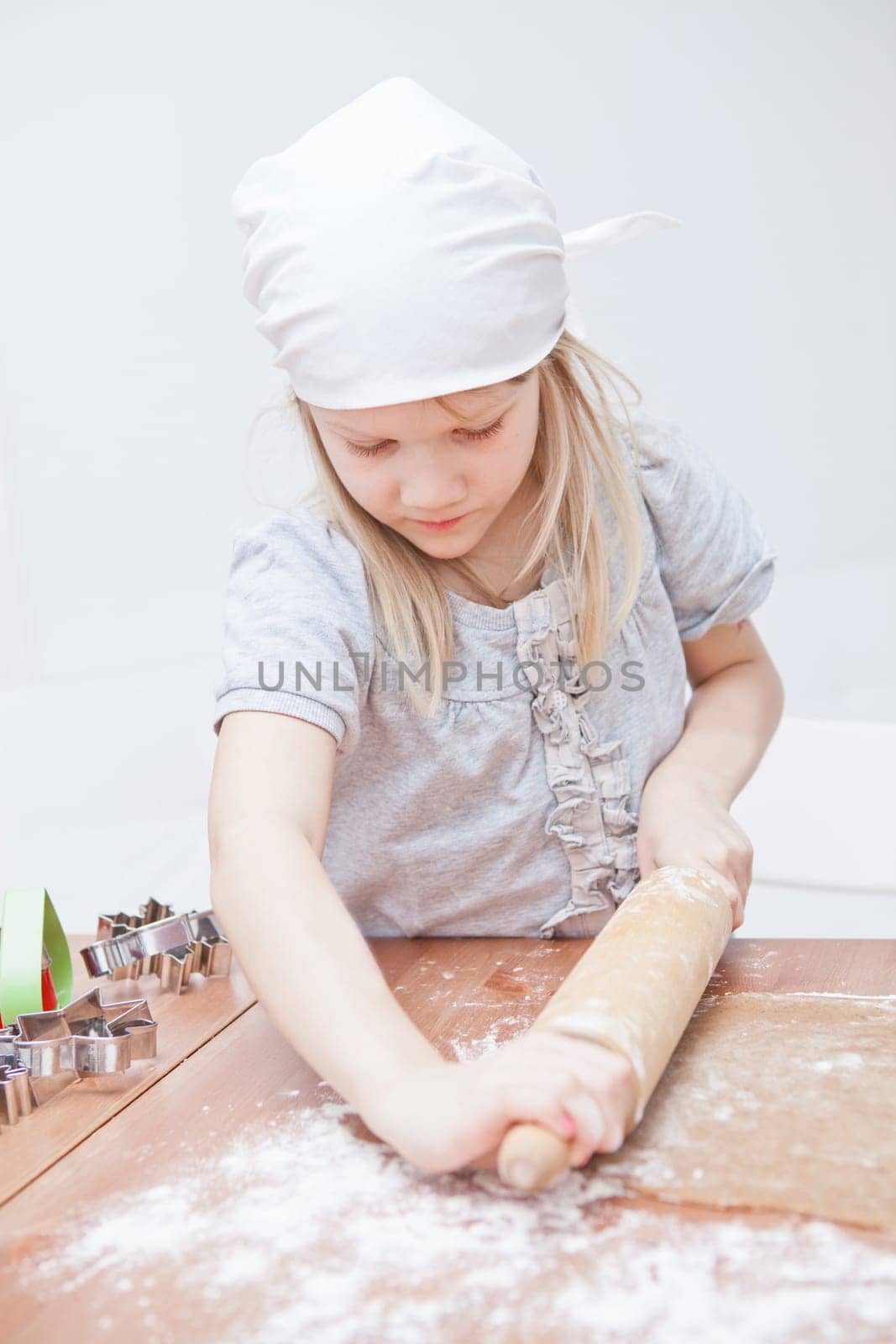 Young girl working on dough with rolling pin to make gingerbread biscuits