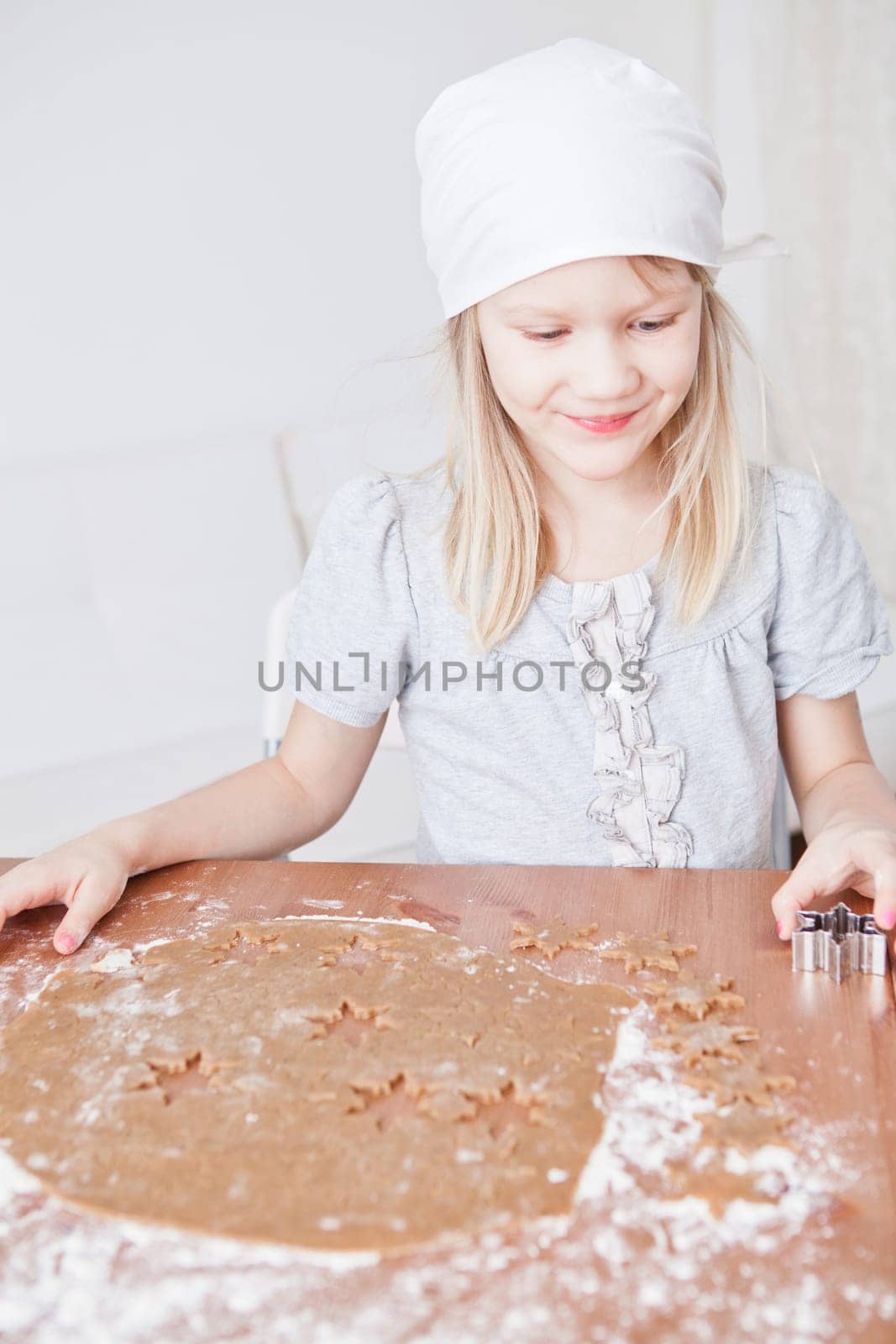 Happy young girl working with dough and shape cutters to make gingerbread biscuits