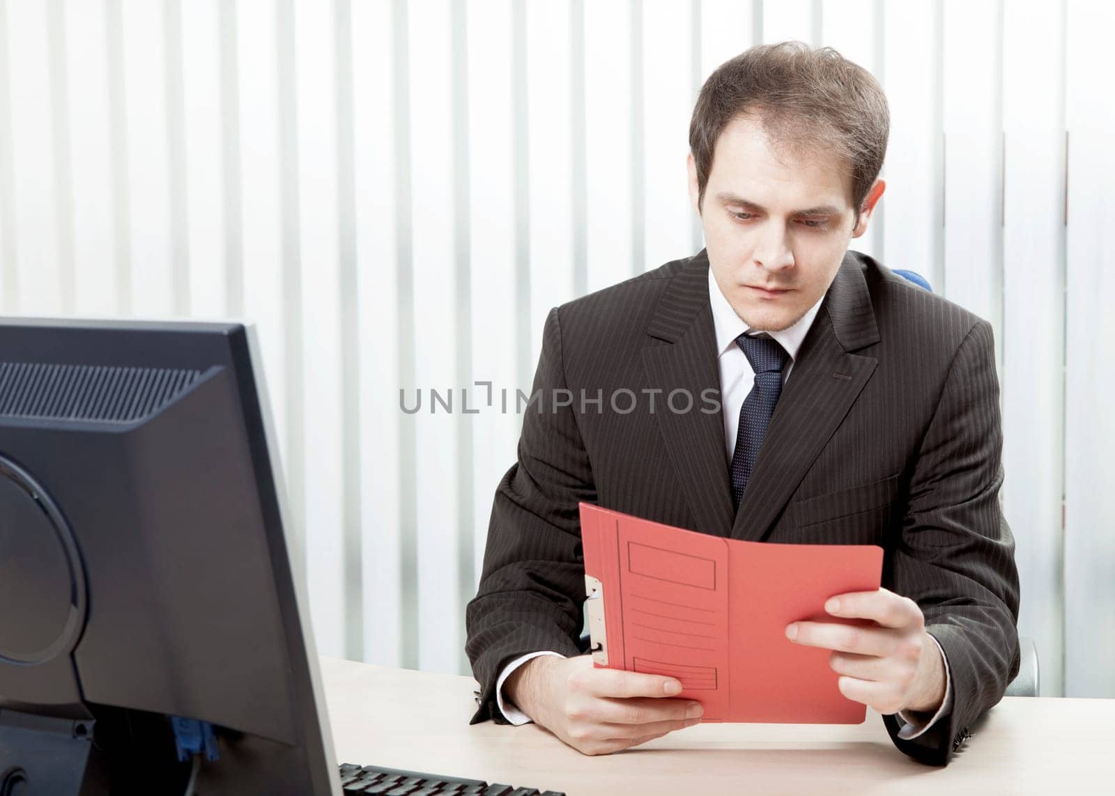 Young worried businessman reading a document at his desk, in his office