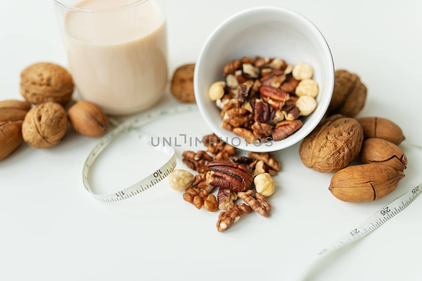 Vegan milk from nuts in a glass cup with various nuts on a white table. Nuts in a bowl. Low-calorie milk for body support