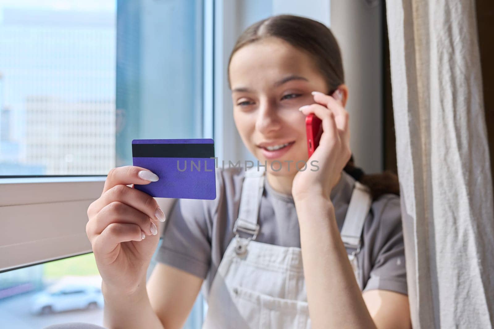 Close-up of credit bank card in hands of young teenage girl with smartphone. Online payment for goods and services, shopping, credit cards for students teenagers concept