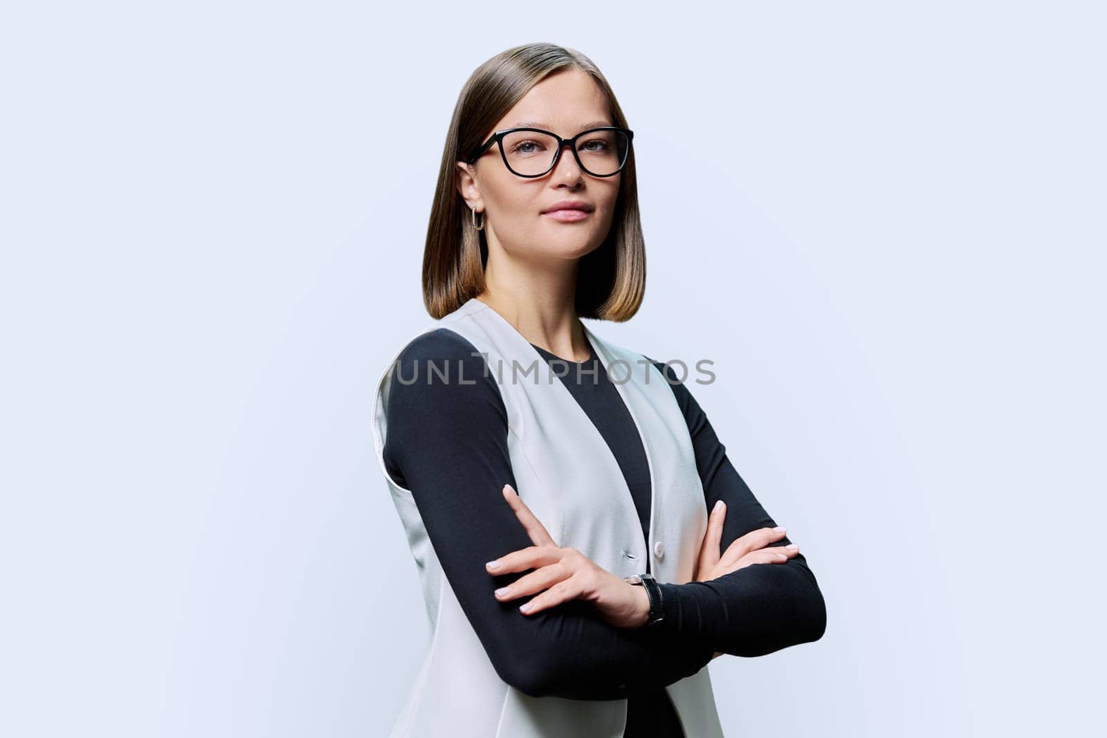 Serious confident young woman with eyeglasses, crossed arms posing on white studio background. Attractive female in black and white clothes. Beauty fashion style youth business job work staff employee