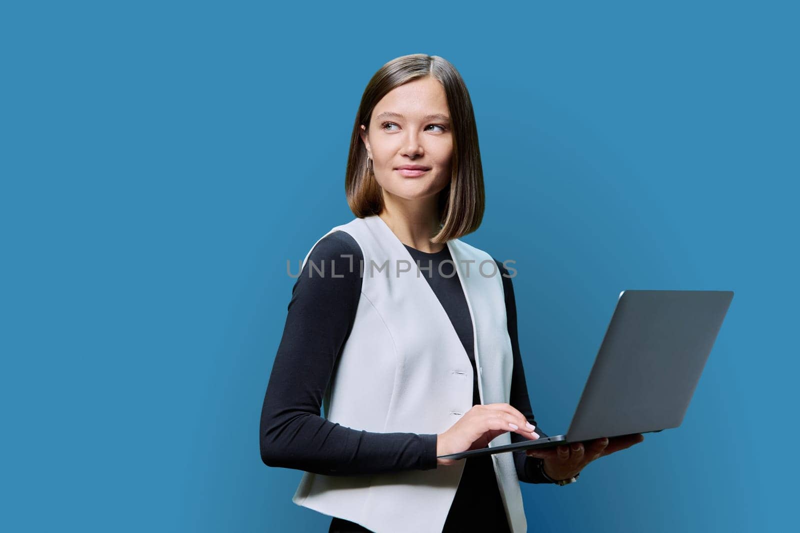 Young woman using laptop computer on blue studio background. Serious female looking to side. Technologies in work business study leisure communication, online Internet applications, lifestyle people