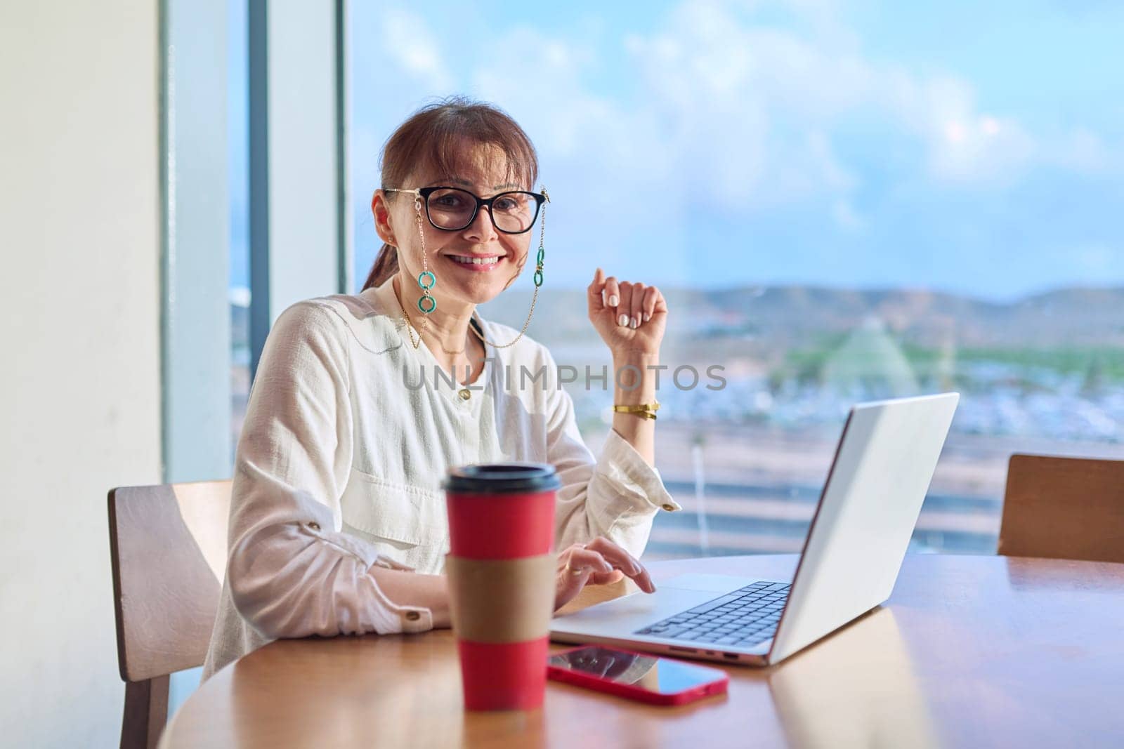 Middle aged woman in airport cafe working with laptop computer by VH-studio