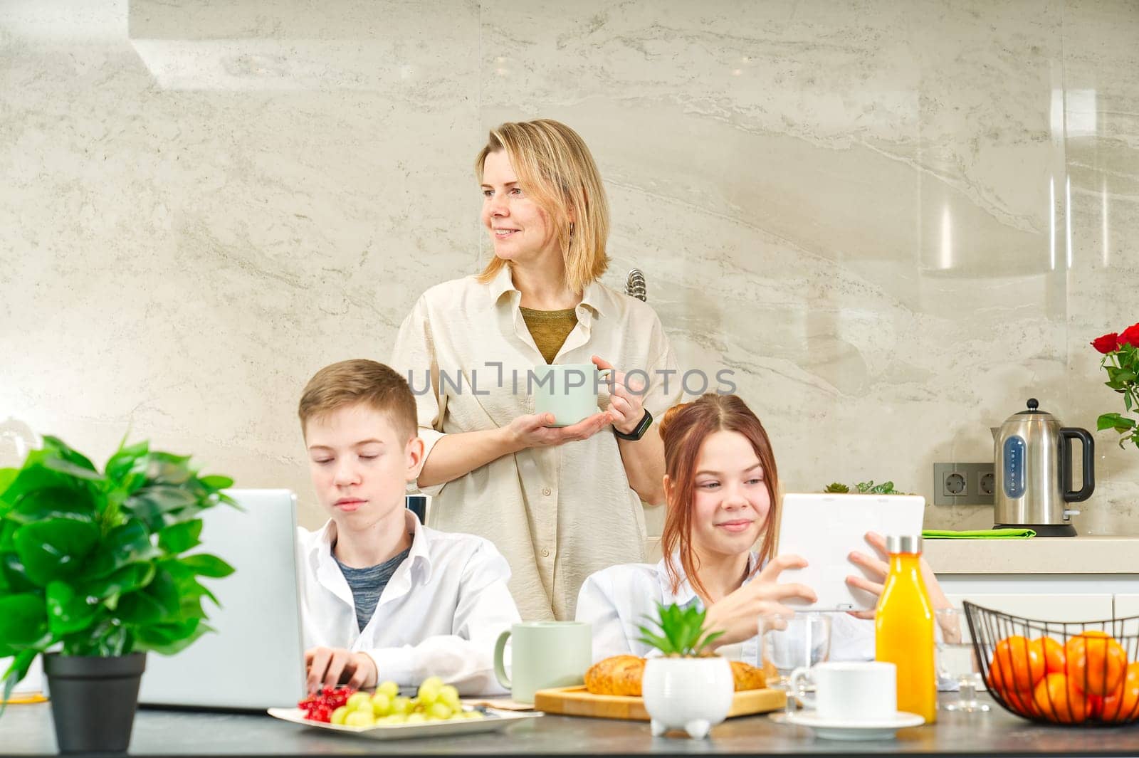 Young family with school kids have fun at breakfast time. Happy family eating healthy breakfast. Quality time with Family in kitchen eating together. Family Using Digital Devices At Breakfast