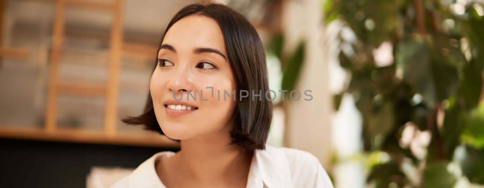 Close up portrait of beautiful, romantic young asian woman, smiling and looking happy, sitting in cozy cafe. Copy space