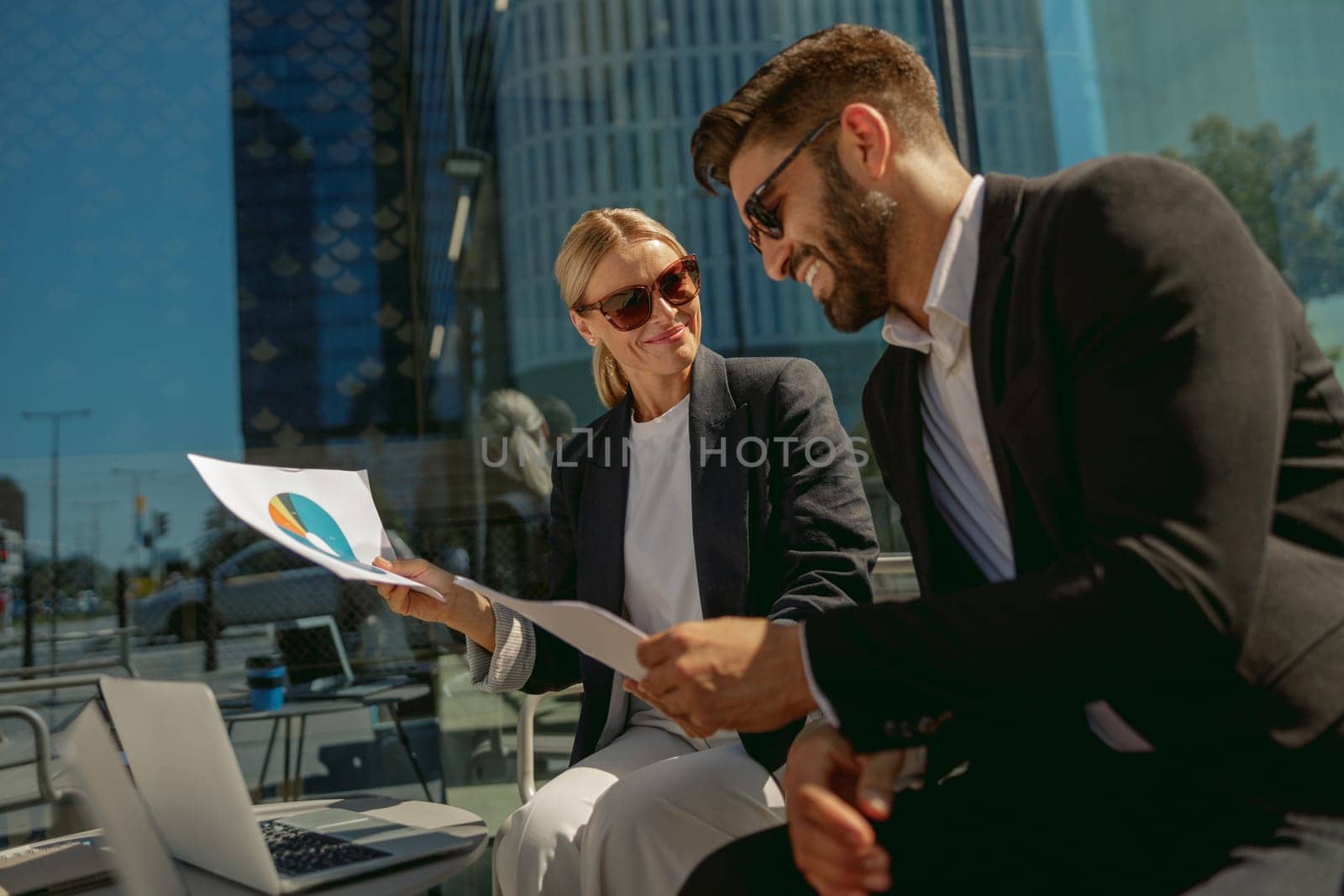 Two business partners working with documents sitting outside of office on cafe terrace by Yaroslav_astakhov