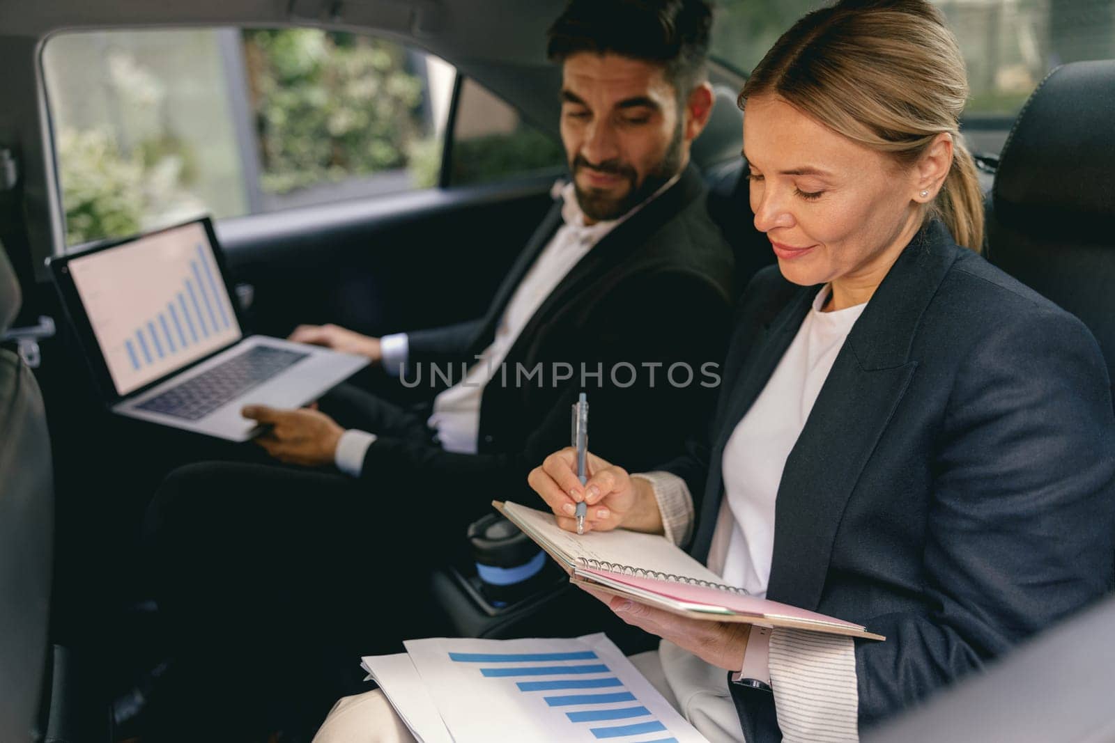 Business colleagues working on laptop and making notes while sitting in car backseats by Yaroslav_astakhov