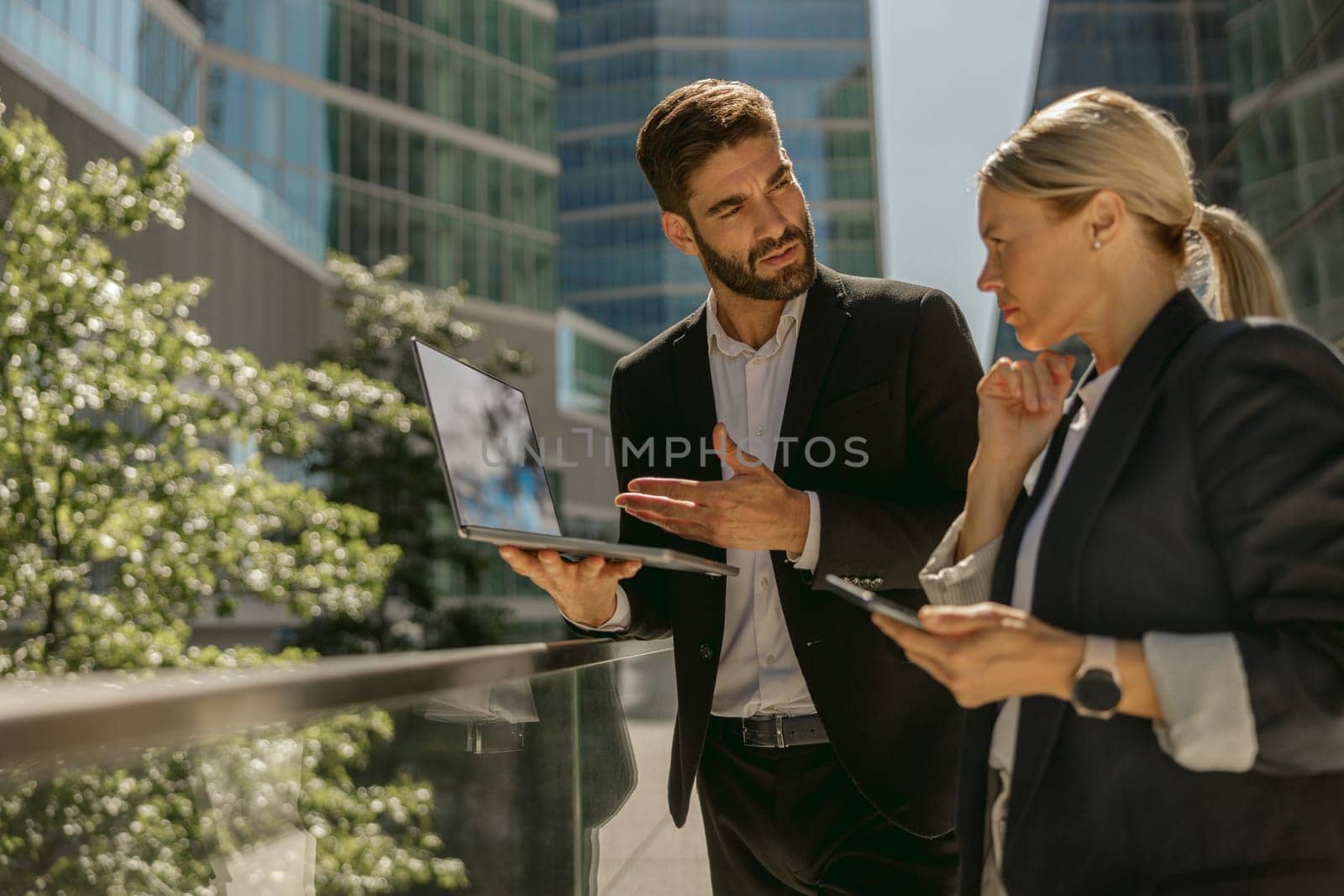 Focused business colleagues discuss biz issue while use laptop standing on office terrace by Yaroslav_astakhov