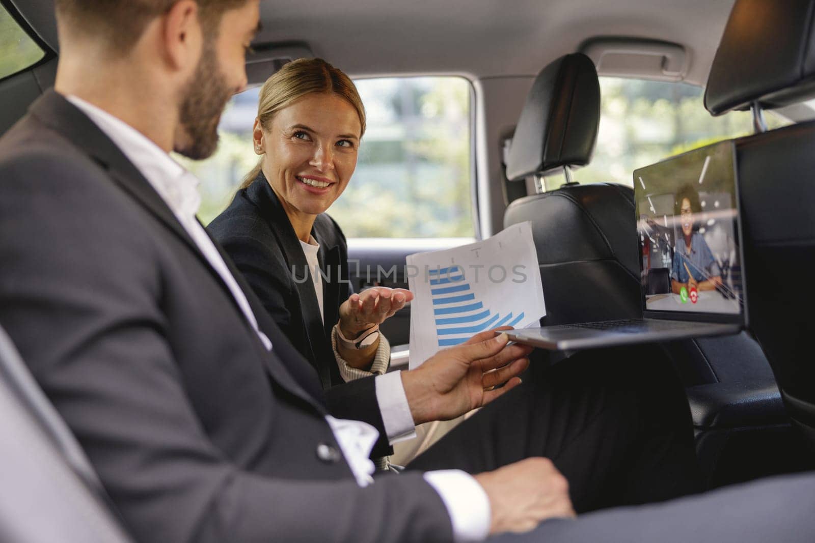 Business colleagues working with documents during video conference in back seat of car by Yaroslav_astakhov