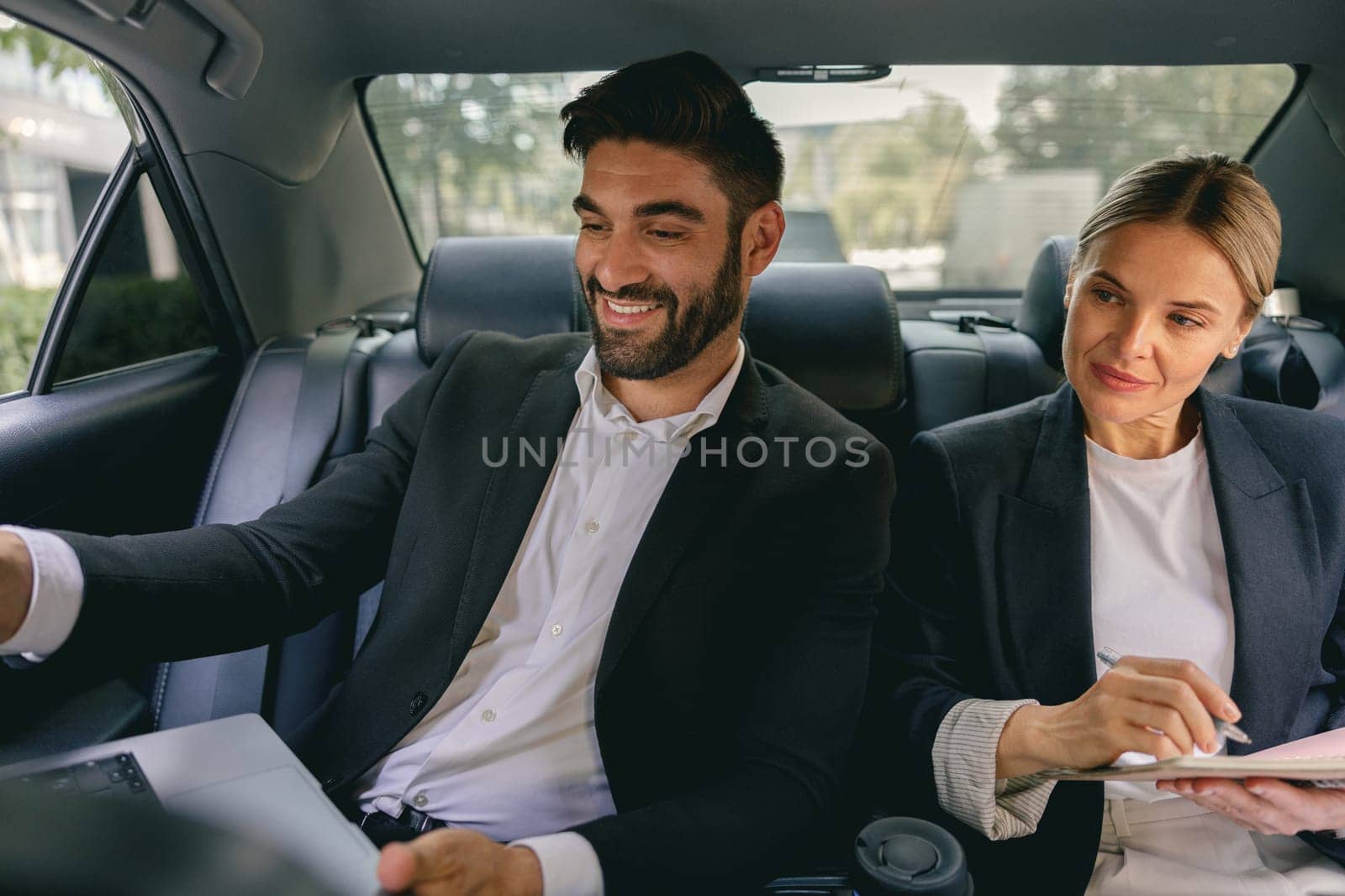Smiling business analysts have online meeting using laptop while sitting in car back seats by Yaroslav_astakhov