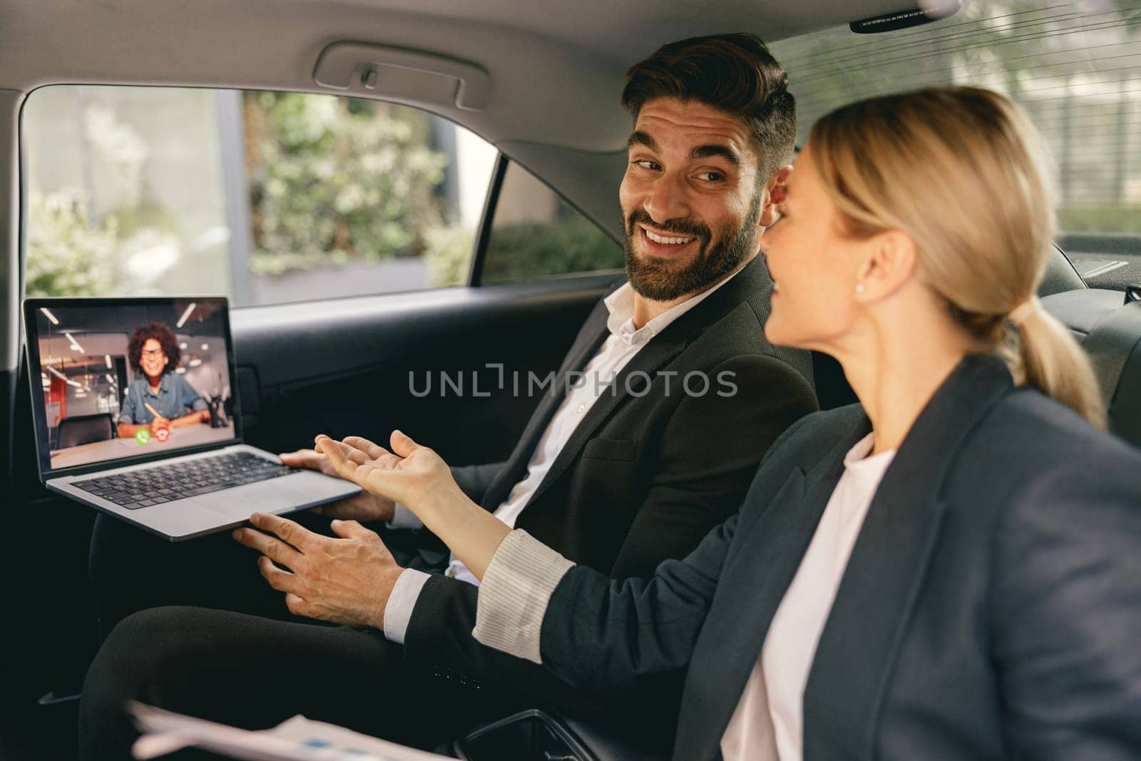 Cheerful business people have online meeting using laptop while sitting in car back seats