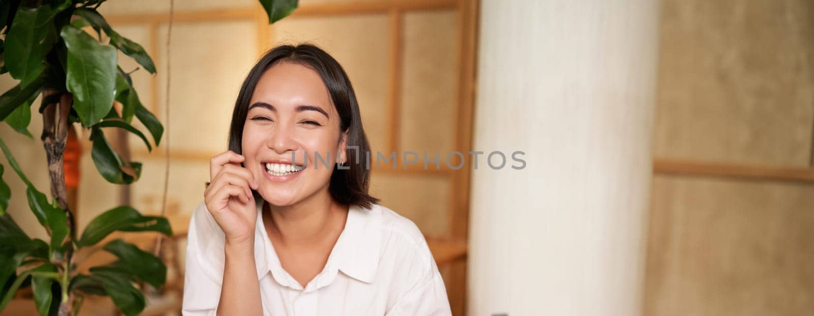 Stylish young woman in cafe with coffee, holding mobile phone, laughing and smiling. Lifestyle and people concept by Benzoix