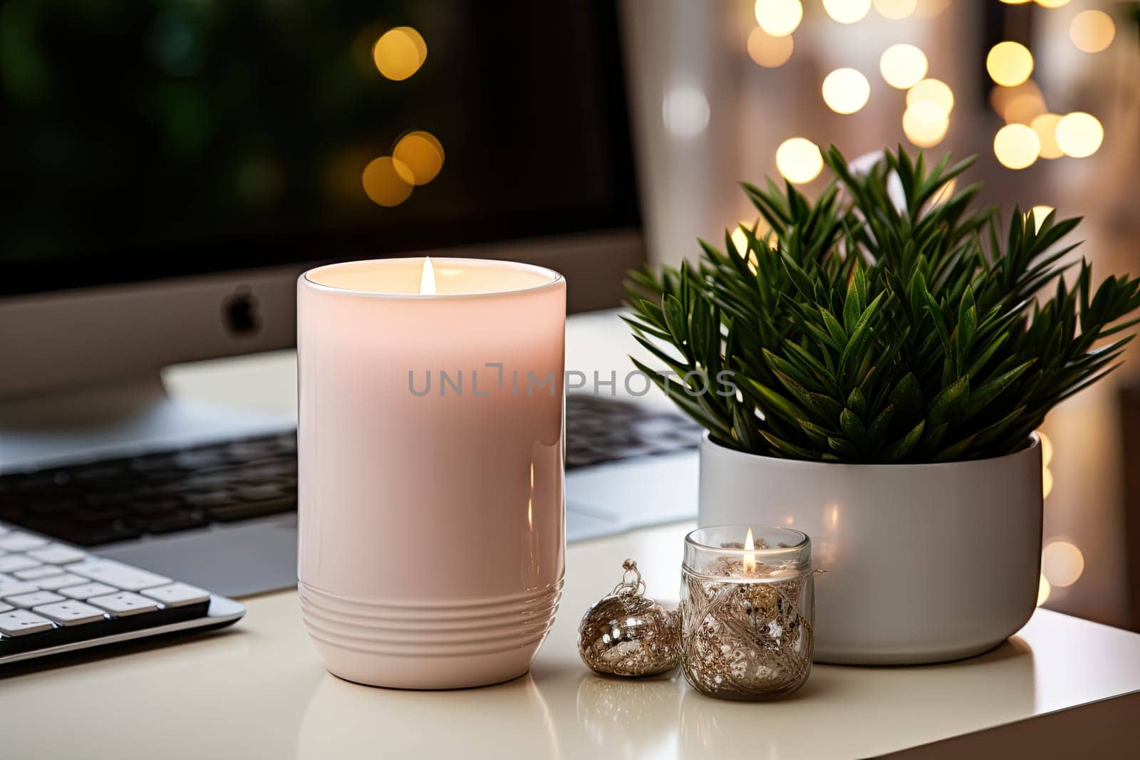 a plant on a desk next to a laptop and a lit candle in front of a computer screen with christmas lights behind it
