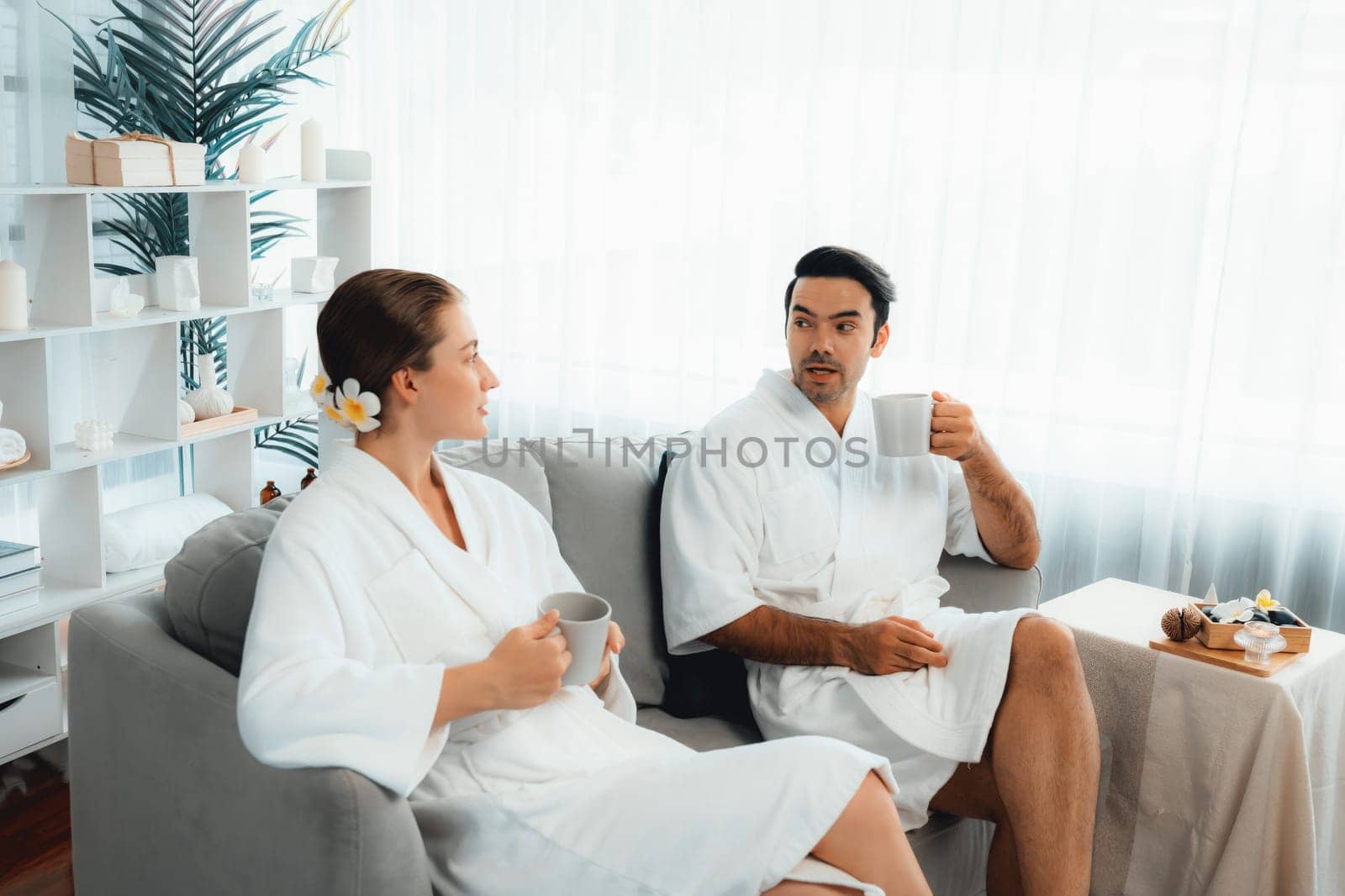 Beauty or body treatment spa salon vacation lifestyle concept with couple wearing bathrobe relaxing with drinks in luxurious hotel spa or resort room. Vacation and leisure relaxation. Quiescent