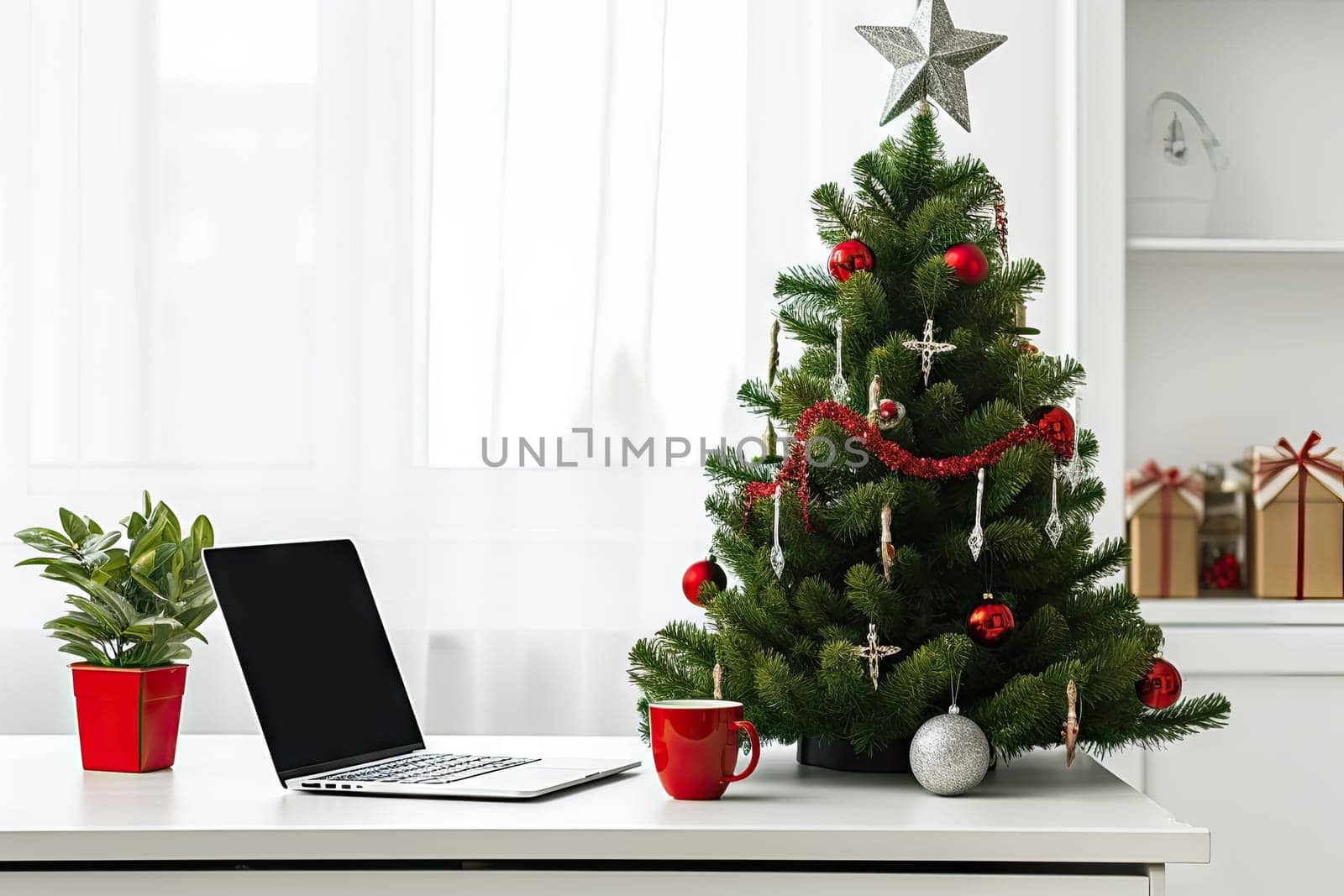 a christmas tree on a desk with a laptop and other office supplies in the fore - image is taken from above