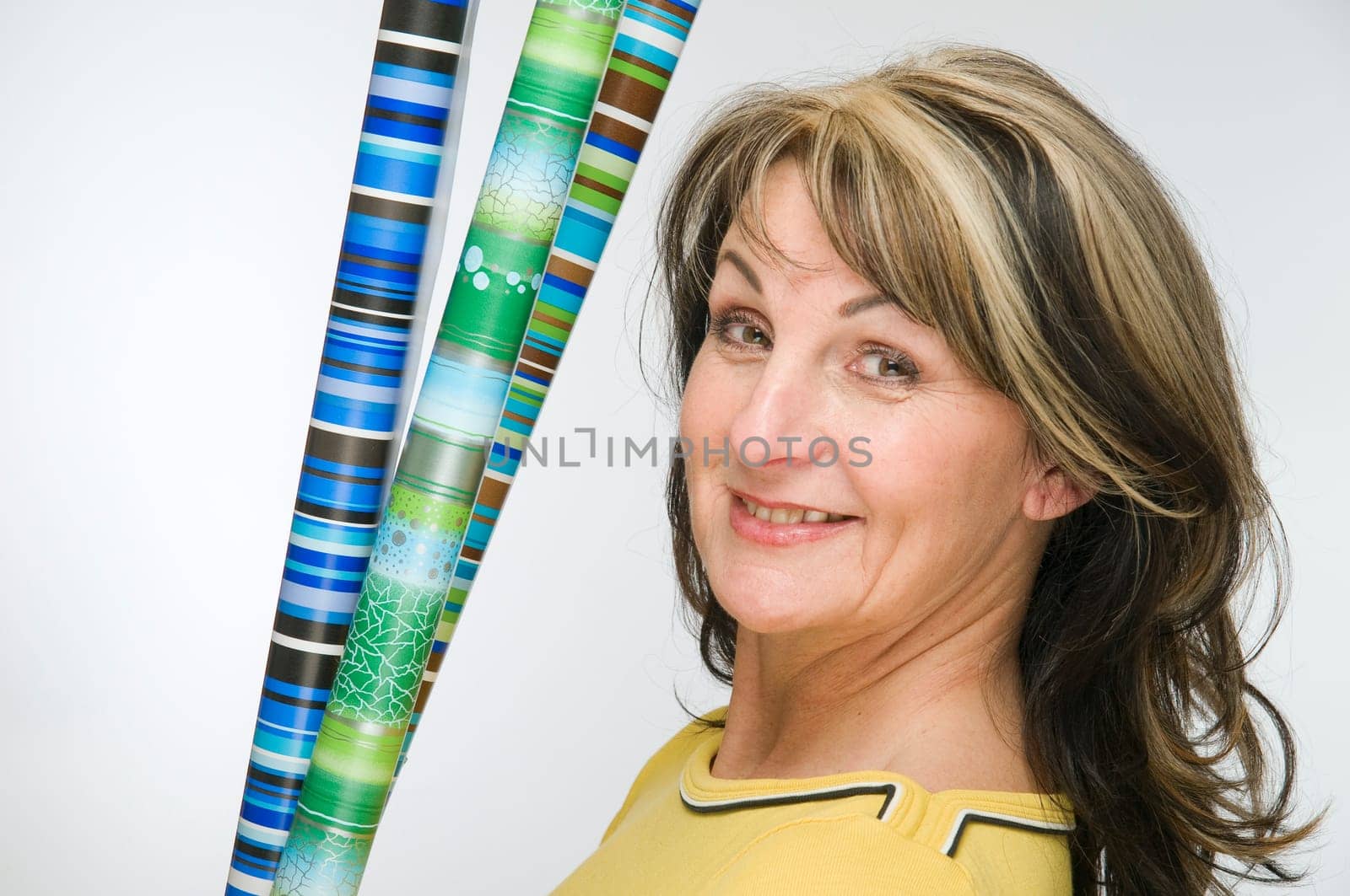 Torso shot of middle-aged woman,yellow sweatshirt and colorful rolls of wrapping paper against light studio background