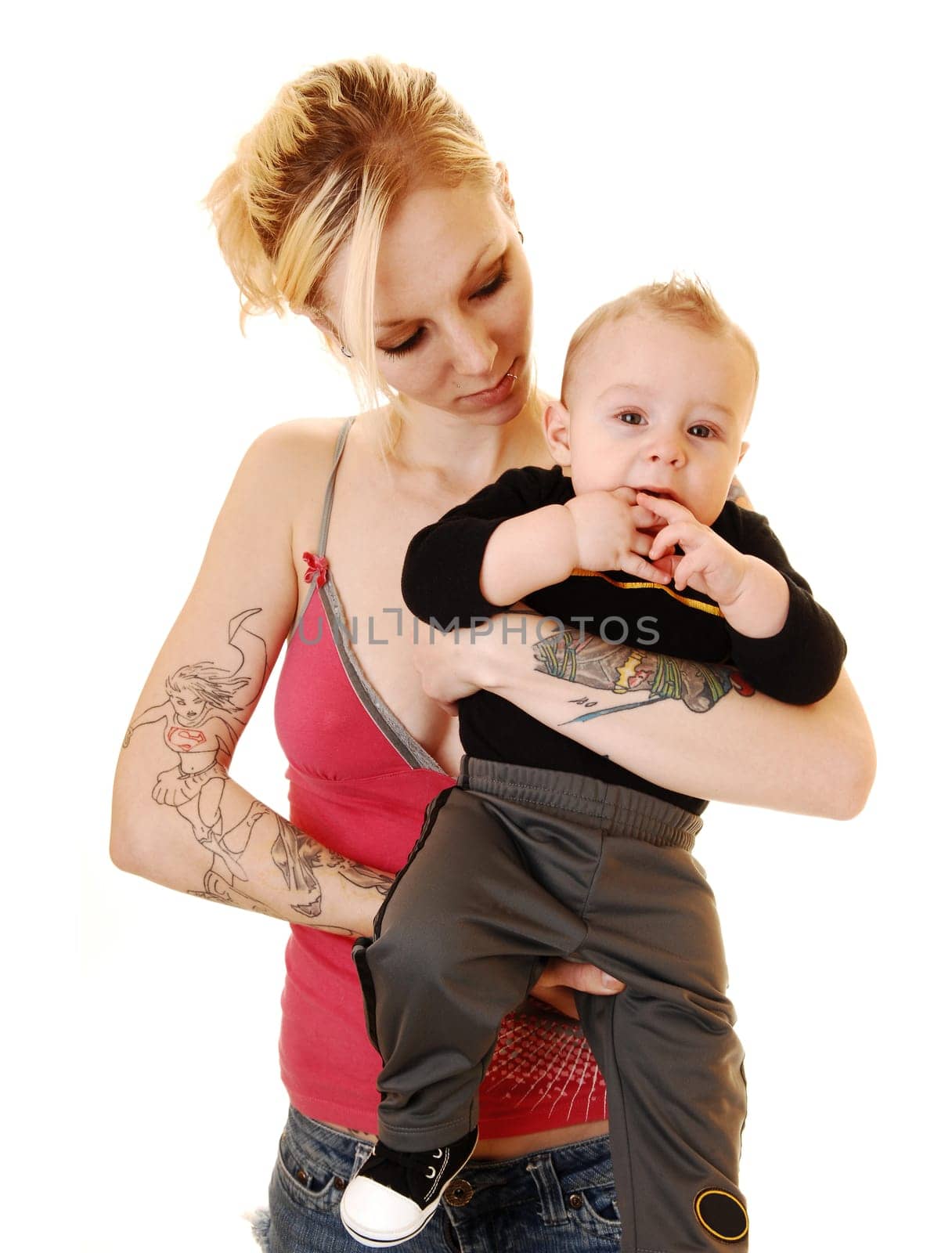 A young baby boy in the arms of his mother, a blond woman with tattoo on her body, standing in the studio for white background.