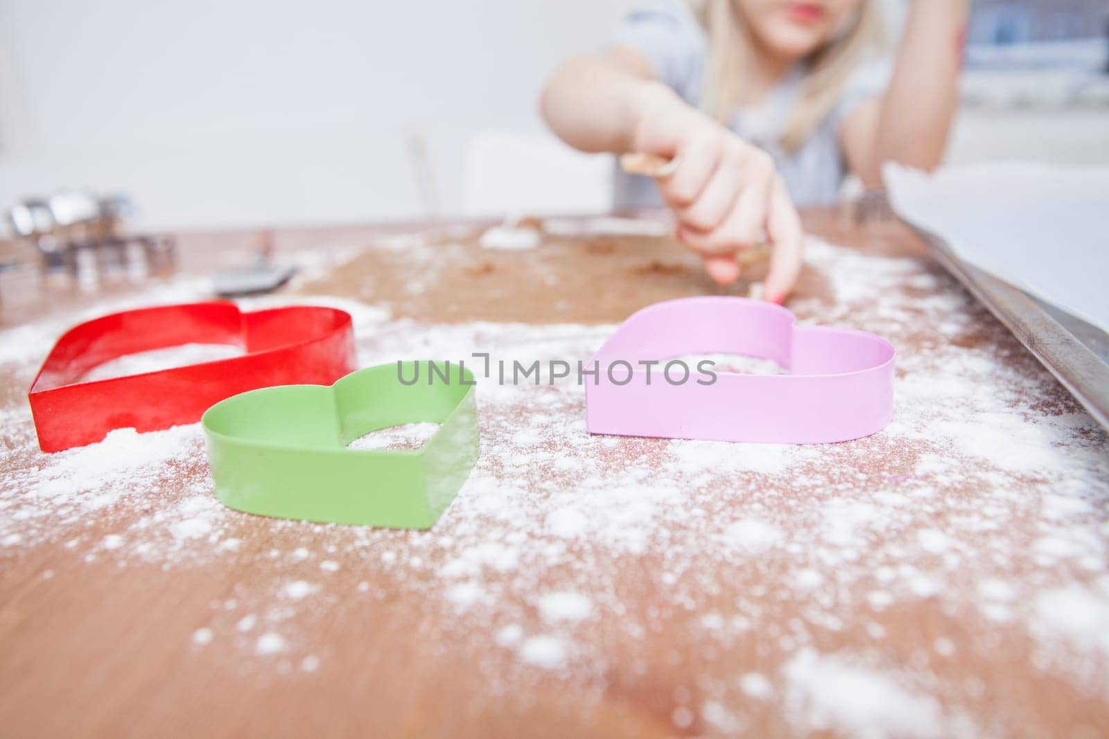 Young girl preparing gingerbread biscuit dough with heart shaped cutters in foreground