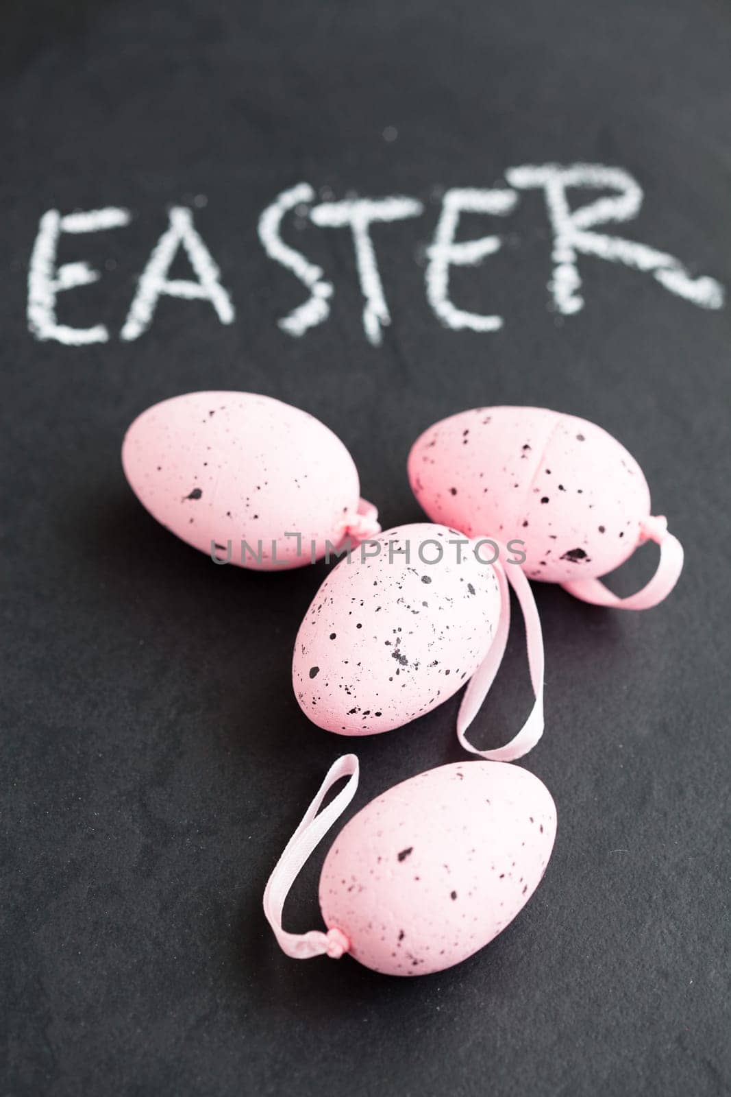 Closeup of four pink spotty Easter eggs and text written in chalk on dark background