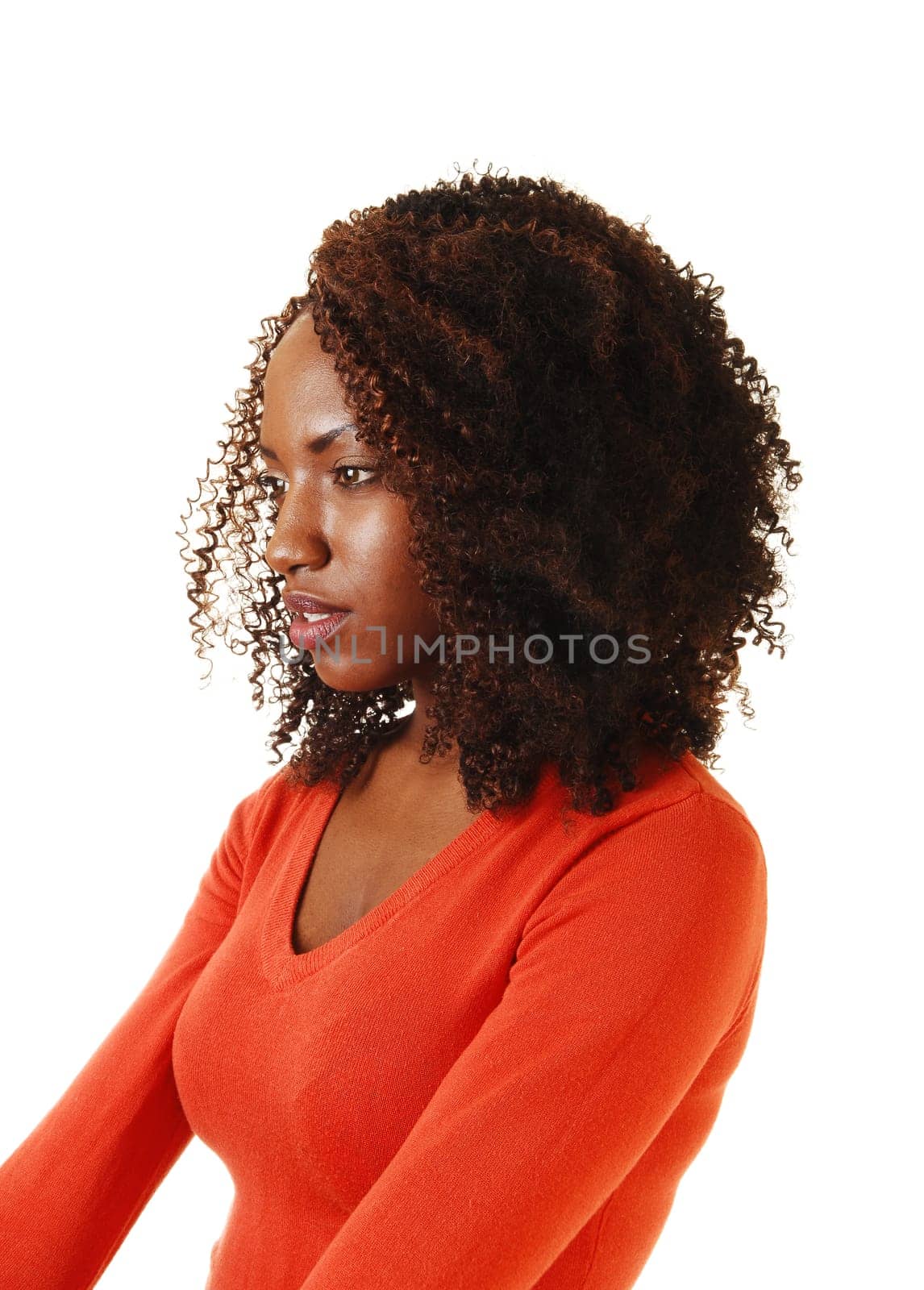 A portrait of a beautiful African American teenager, sitting with her long curly brown hair, in a orange sweater, for white background.