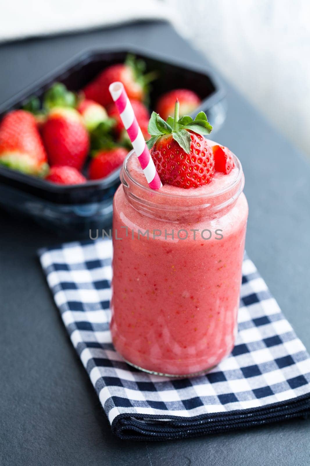 Closeup of strawberry fruit smoothie and tray of fresh strawberries in background