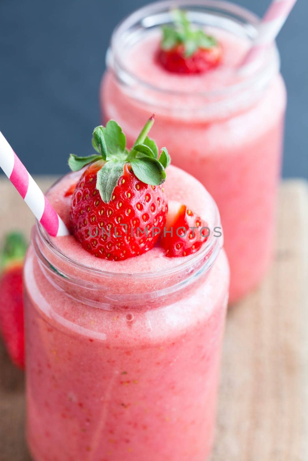 Closeup of strawberry fruit smoothies with strawberry pieces in glass with straw