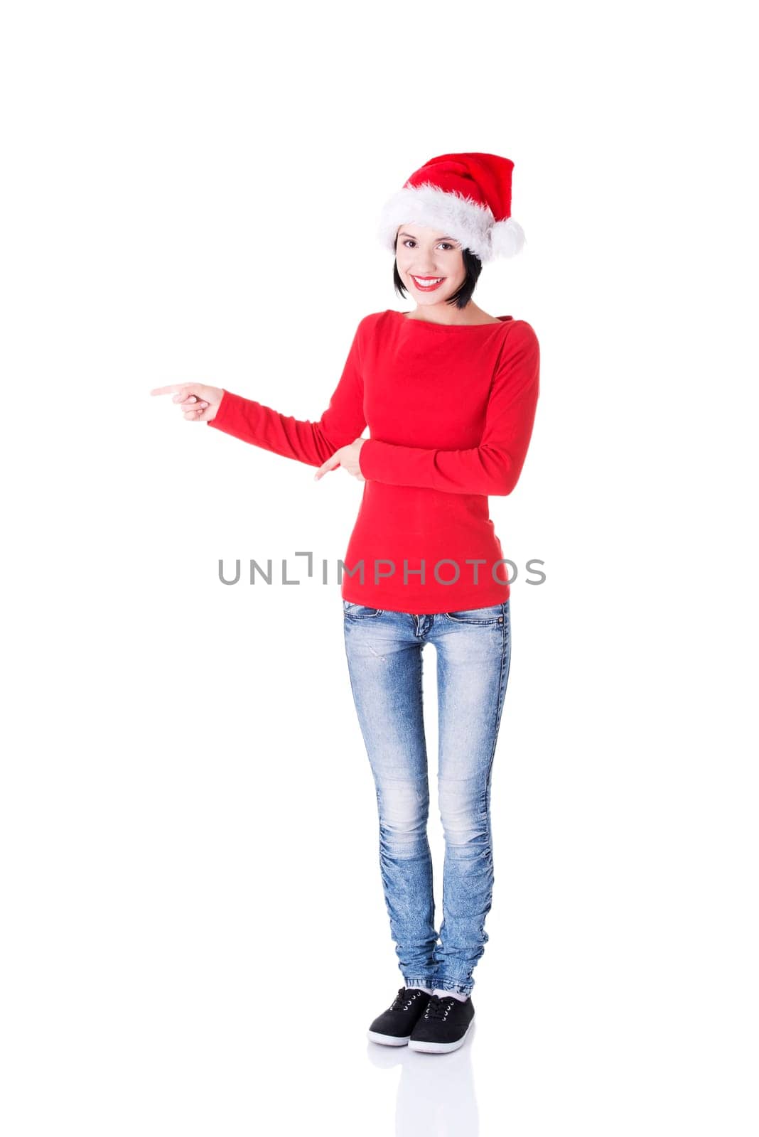 Beautiful smiling christmas santa woman pointing on side showing copyspace. Isolated on white background.