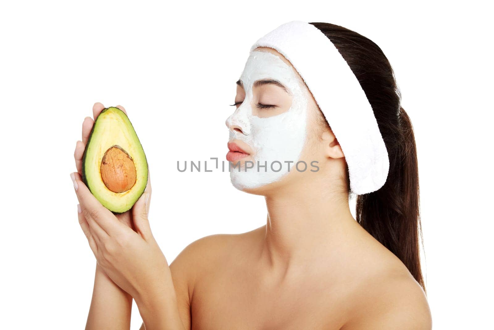 Attractive woman with face clay mask holding avocado. Isolated on white